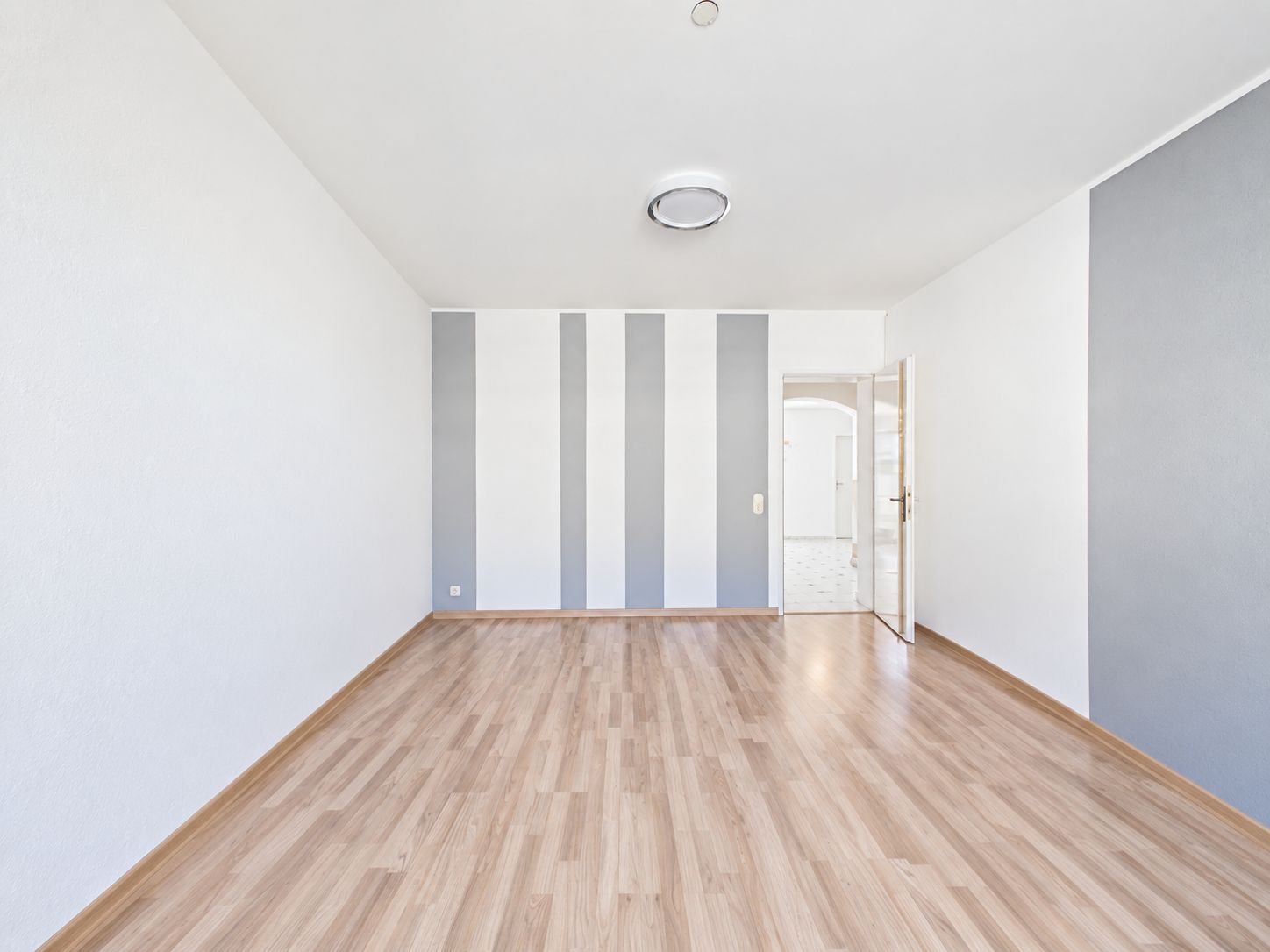 Heller, leerer Raum mit Holzfußboden und weißen Wänden, grauen Streifen und offener Tür.