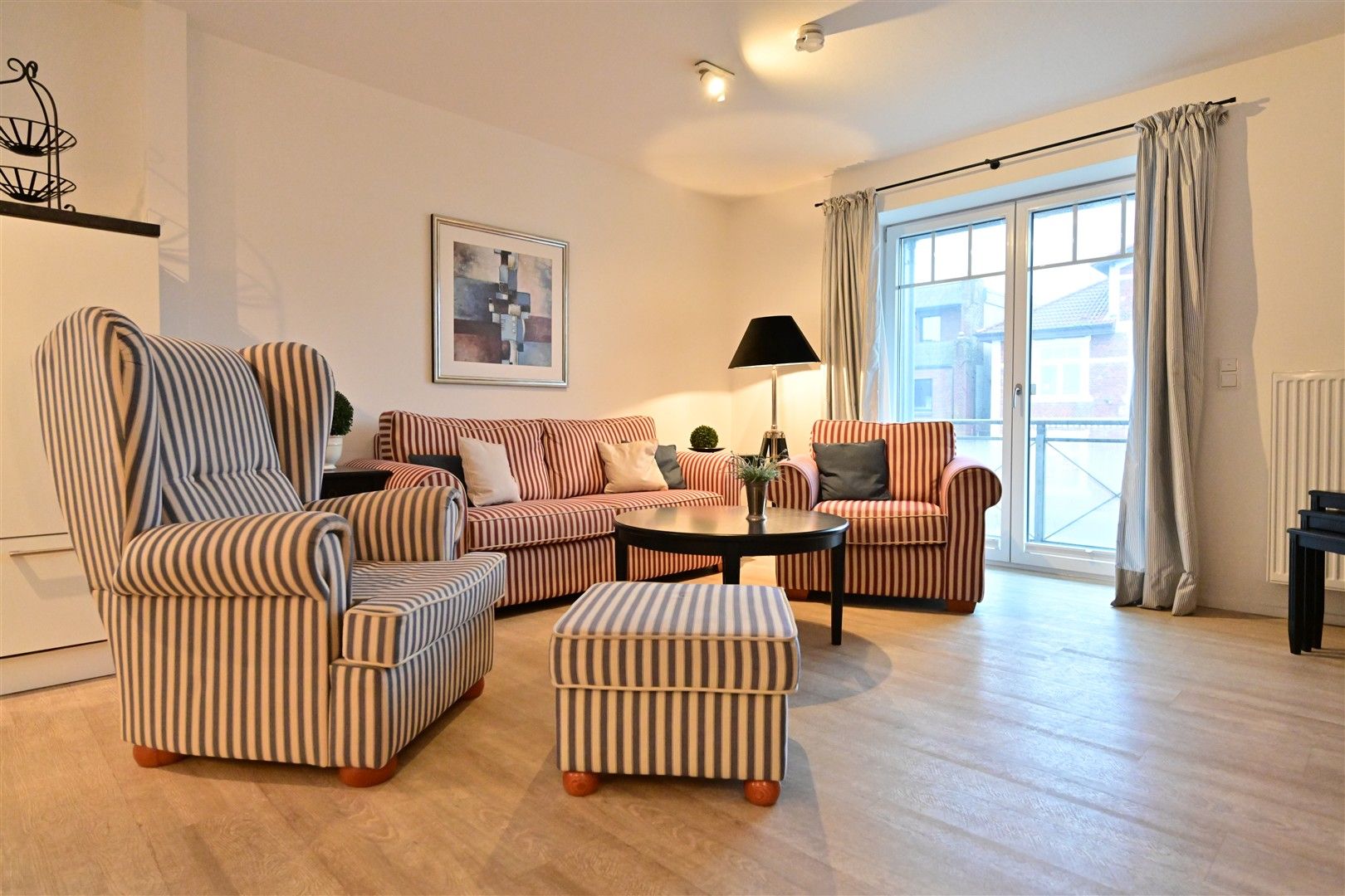 Wohnzimmer mit gestreiftem Sessel, Hocker, Sofa, Couchtisch und großem Fenster.