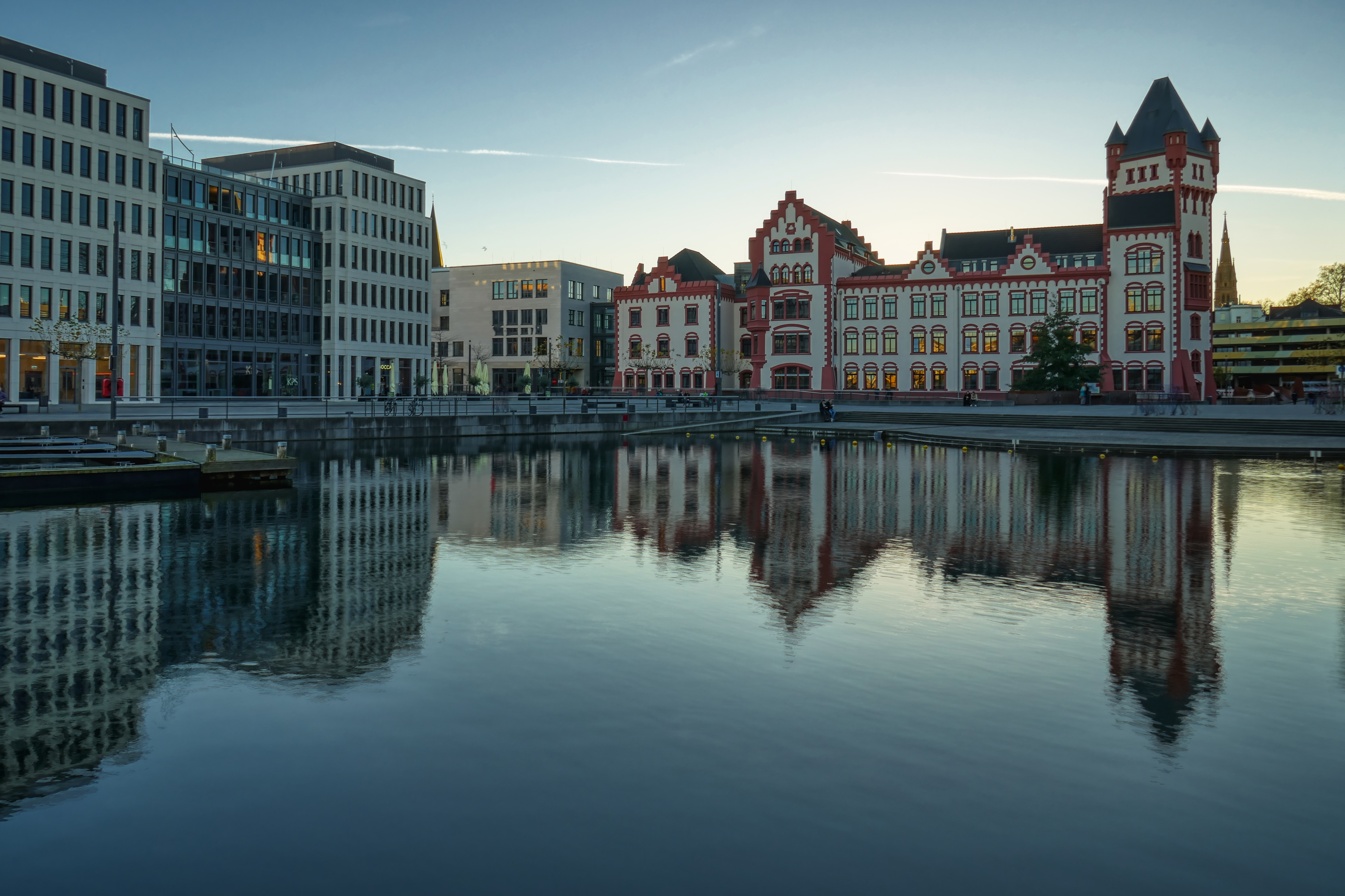 Mehrstöckige Gebäude am Wasser spiegeln sich in der ruhigen Oberfläche eines Kanals.