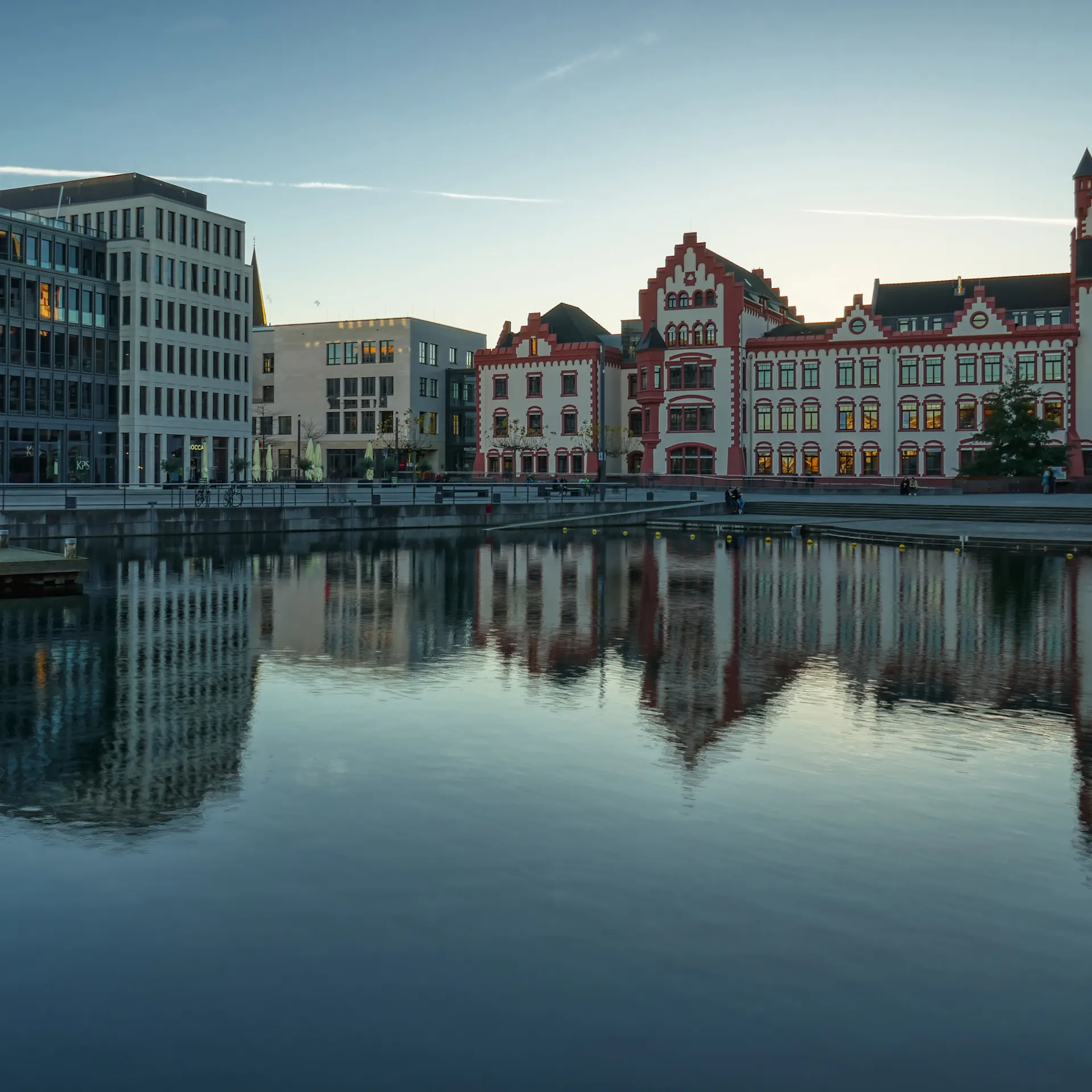 Mehrstöckige Gebäude am Wasser spiegeln sich in der ruhigen Oberfläche eines Kanals.