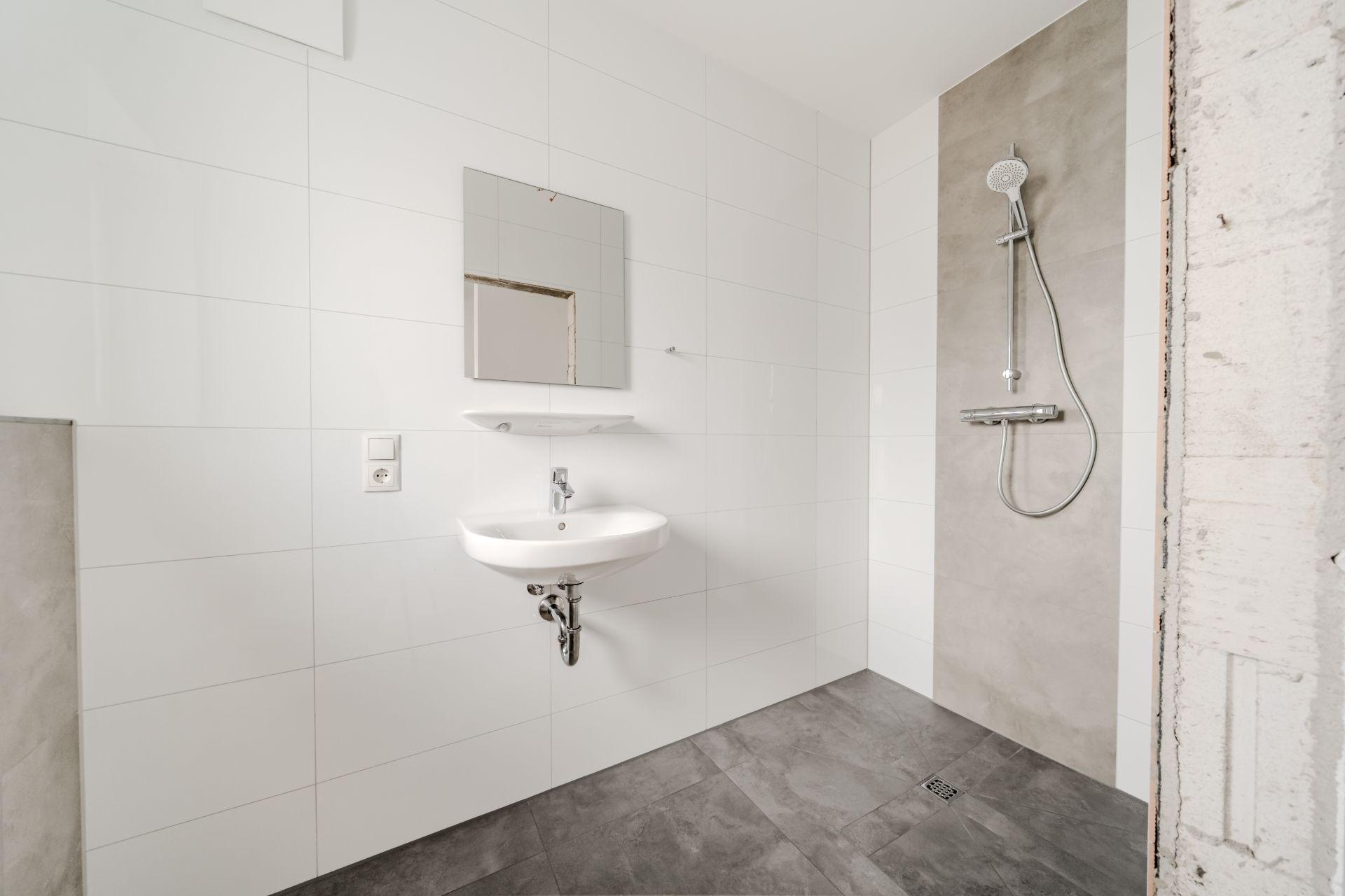 Modernes Badezimmer mit Waschbecken, Spiegel und offener Dusche an der Wand.