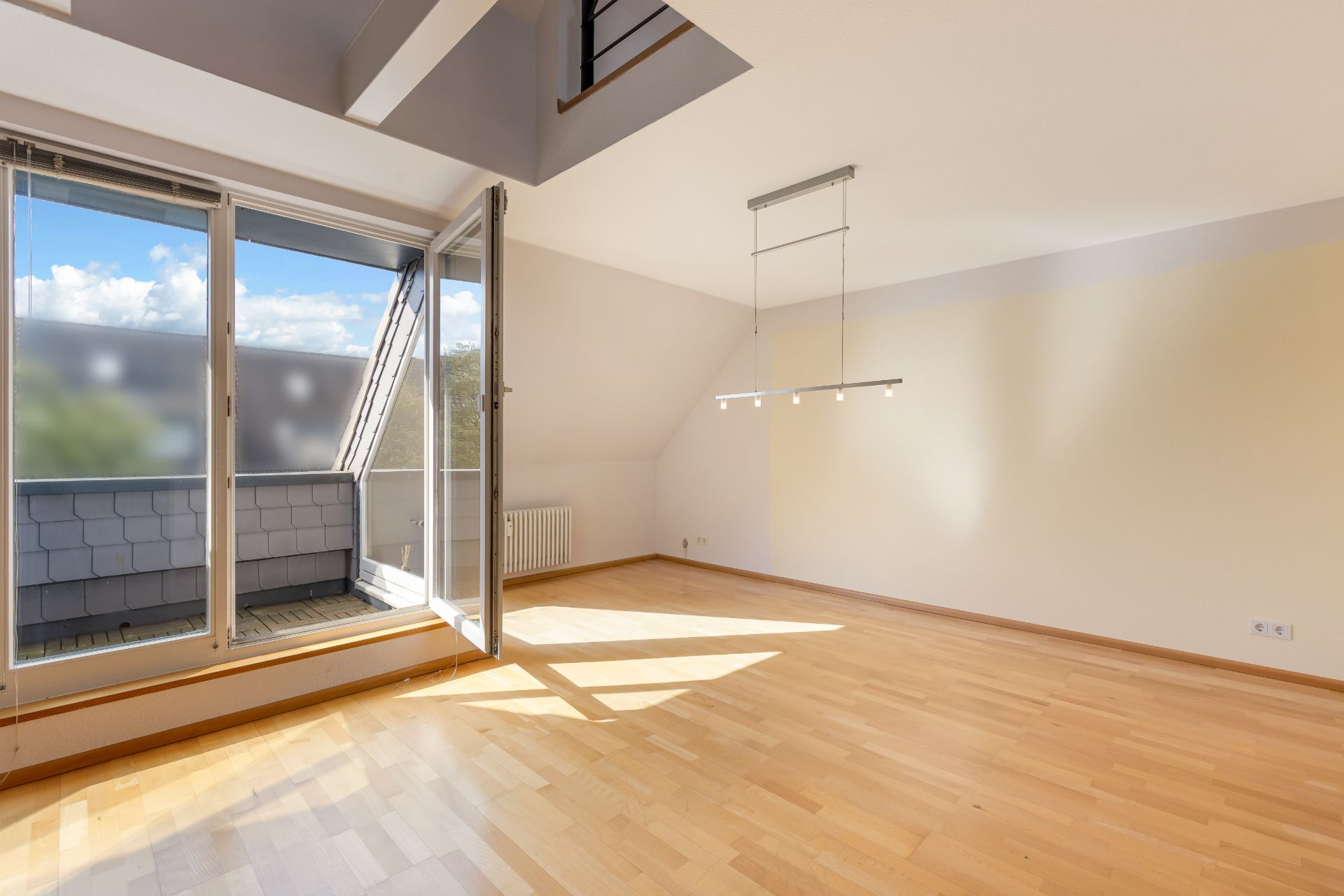 Heller Raum mit Parkettboden, großem Fenster und Zugang zu einem kleinen Balkon.