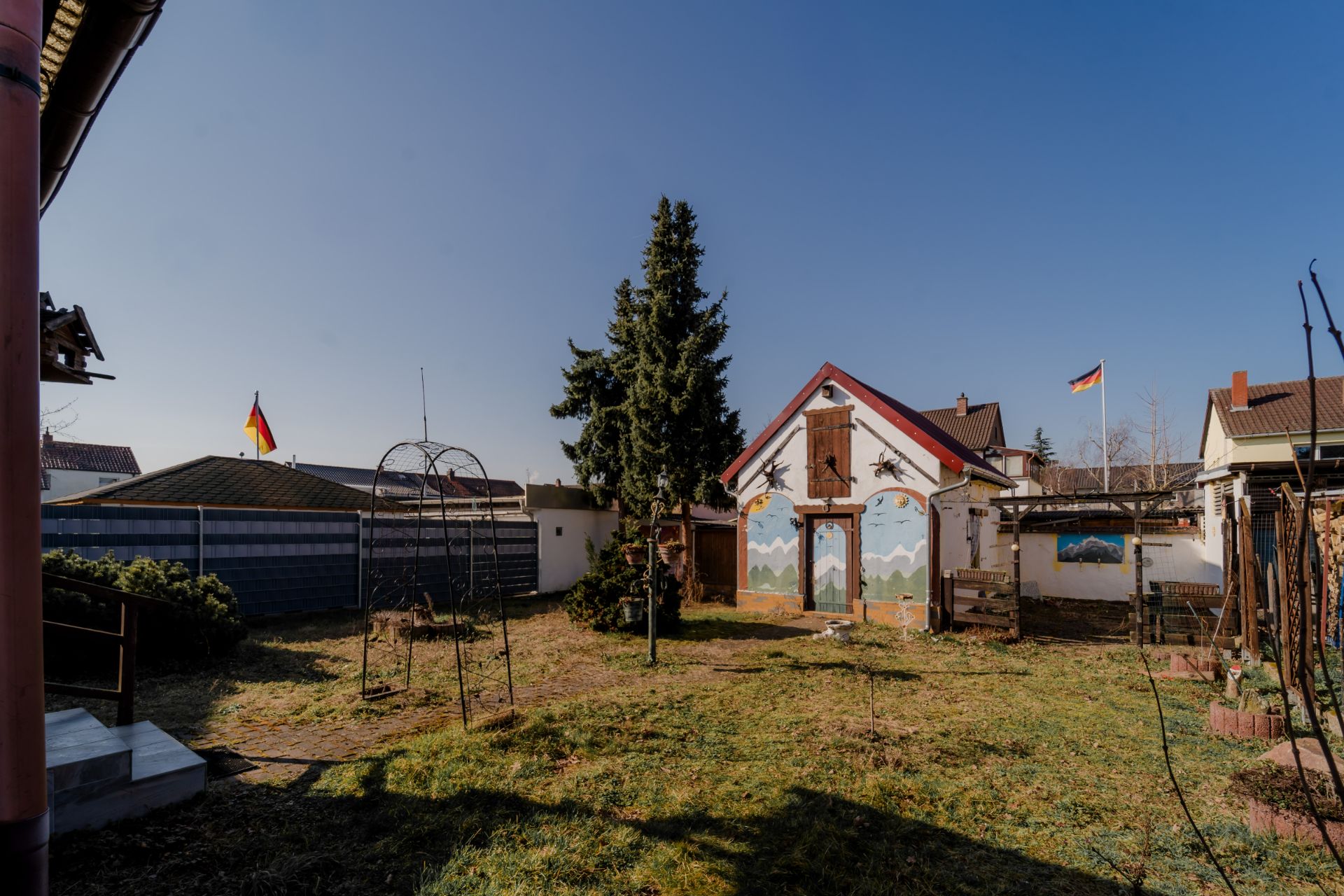Garten mit Rasen, Baum in der Mitte, Haus mit bemalter Wand im Hintergrund.