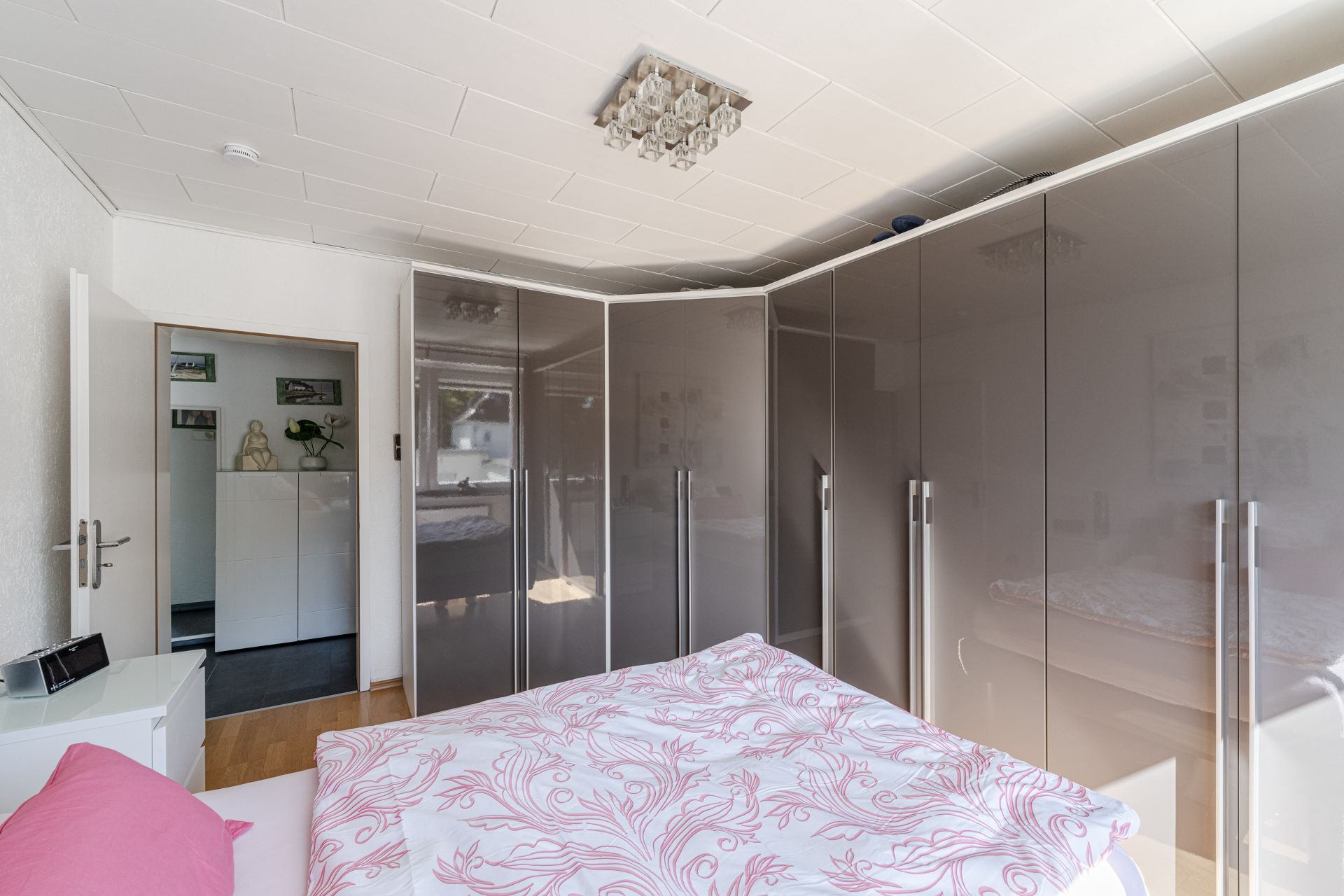Schlafzimmer mit großem Eck-Kleiderschrank, Bett und Nachttisch, helle und moderne Einrichtung.