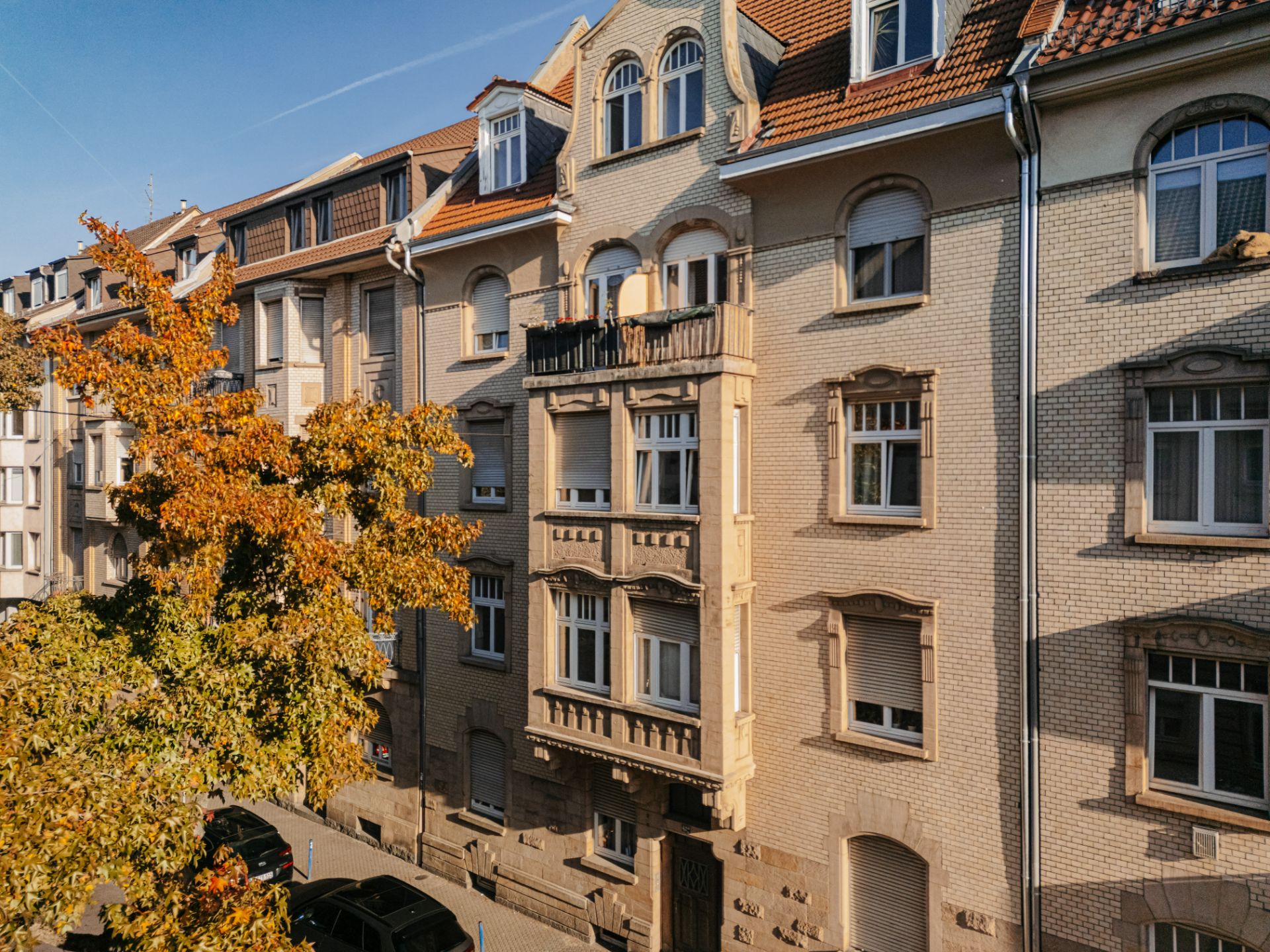 Mehrfamilienhaus mit Balkonen und Herbstbaum im Vordergrund.