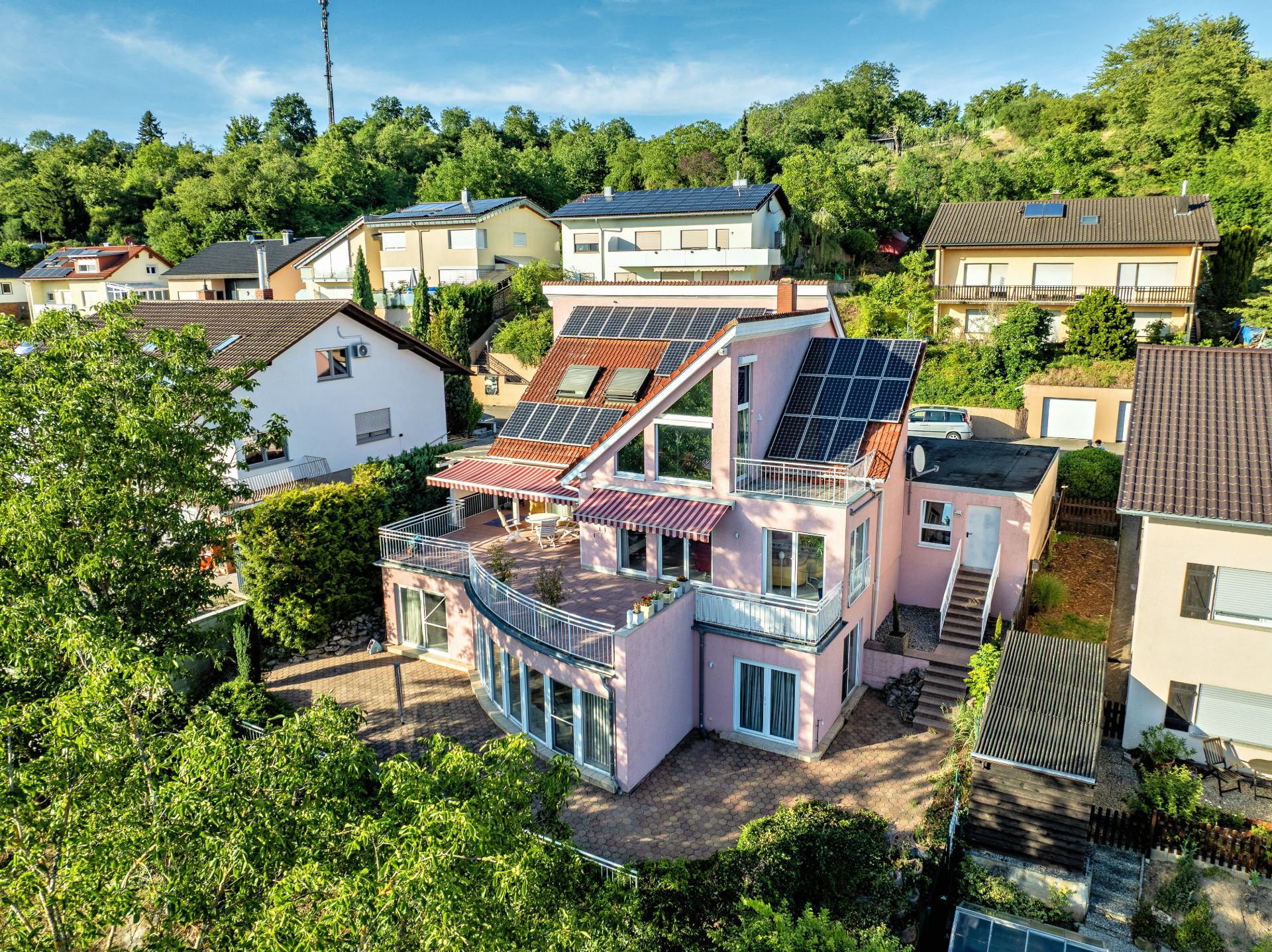 Modernes, rosa Wohnhaus mit großen Fenstern, Terrassen und Solarpanelen auf dem Dach.