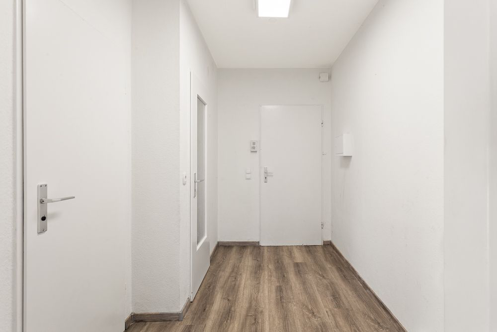 Heller Flur mit weißen Wänden und Holzboden, mehrere Türen sind sichtbar.