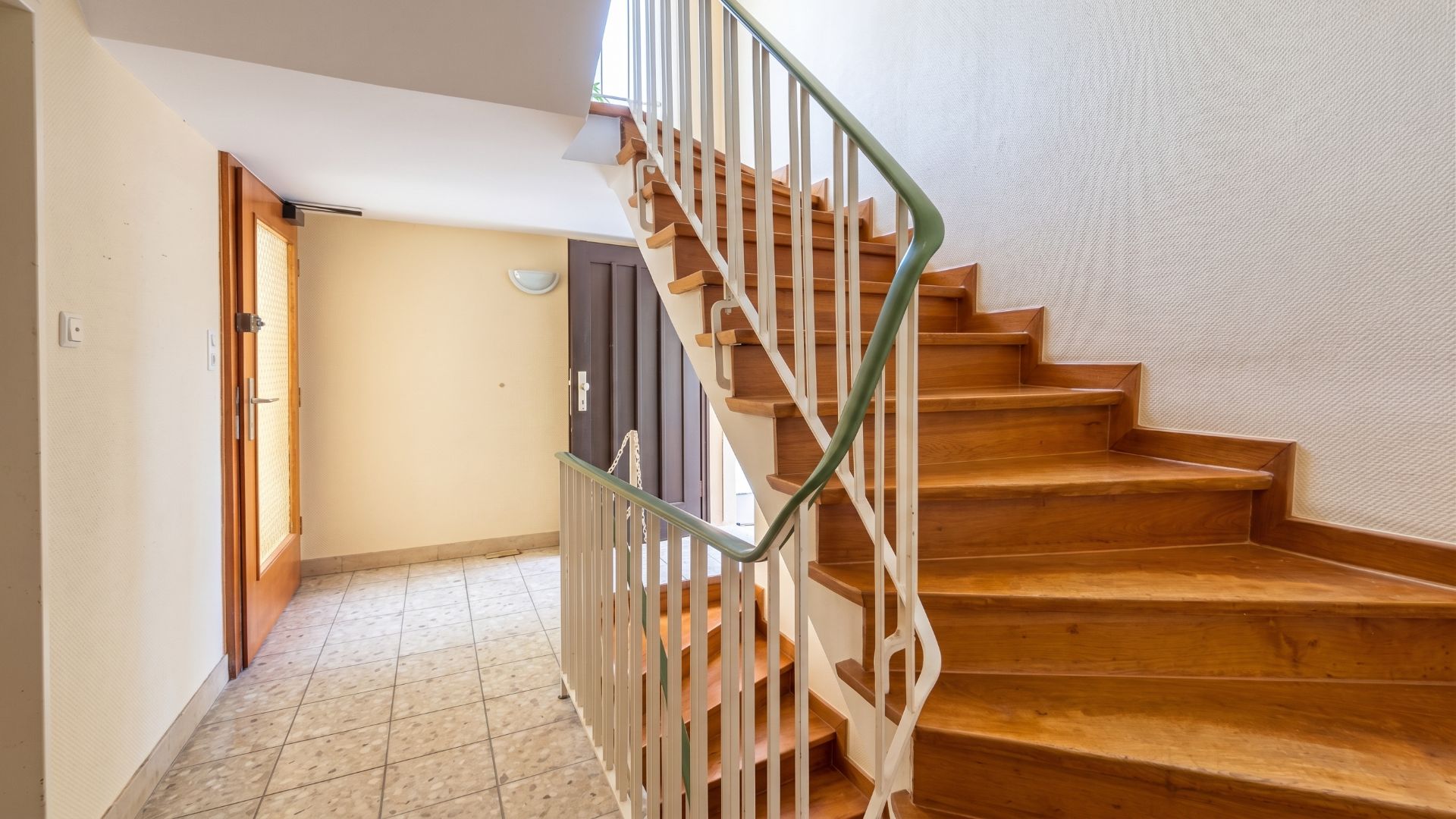 Treppenhaus mit Holztreppe und gefliestem Boden in einem Wohnhaus.