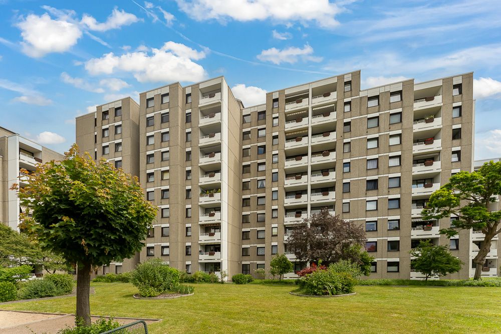 Mehrstöckiges Wohnhaus mit Balkonen und gepflegtem Garten im Vordergrund.