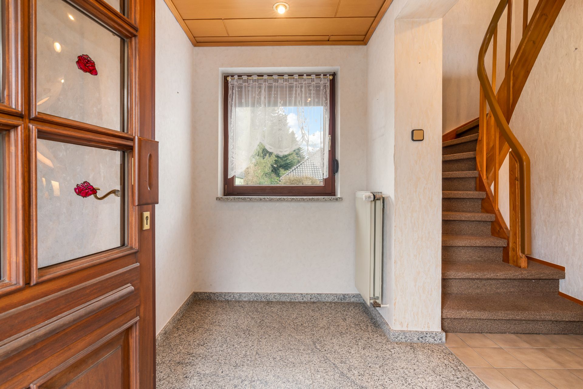 Eingangsbereich mit Holztür, Fenster, Heizung und Treppe mit Holzgeländer.