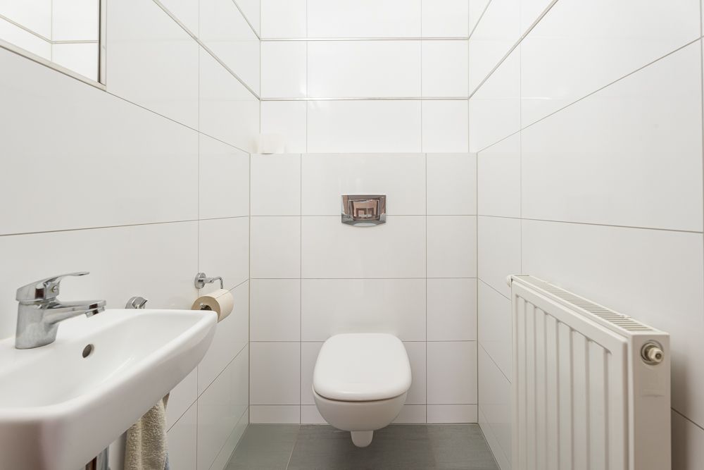 Kleines Badezimmer mit weißem WC, Waschbecken, Handtuch und Heizung an der Wand.