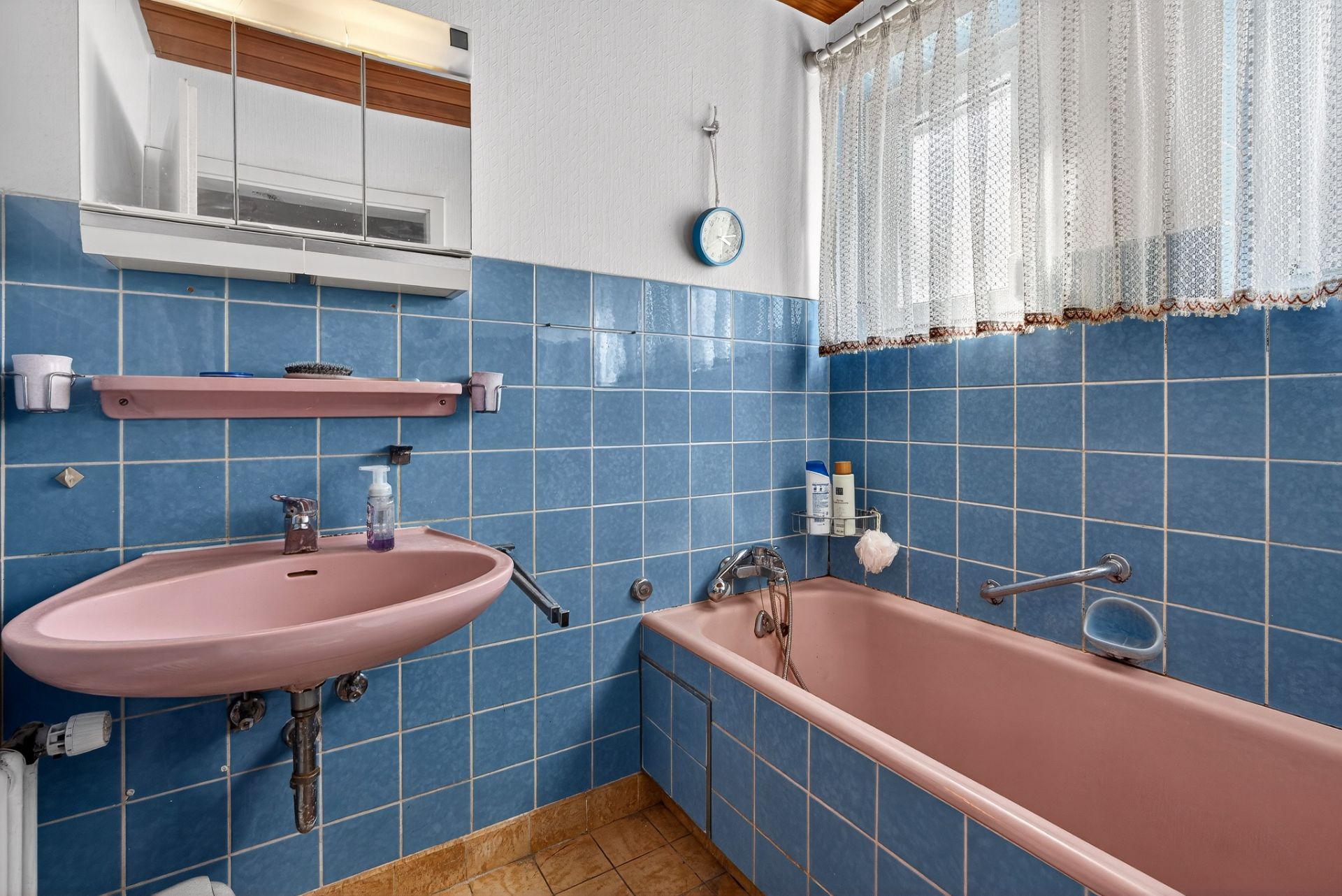 Badezimmer mit rosa Waschbecken und Badewanne, blauen Fliesen und großem Fenster mit Vorhang.