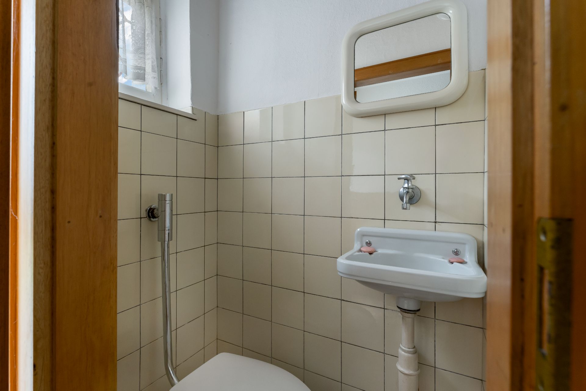 Kleines Badezimmer mit Toilette, Waschbecken, Spiegel und Fenster.
