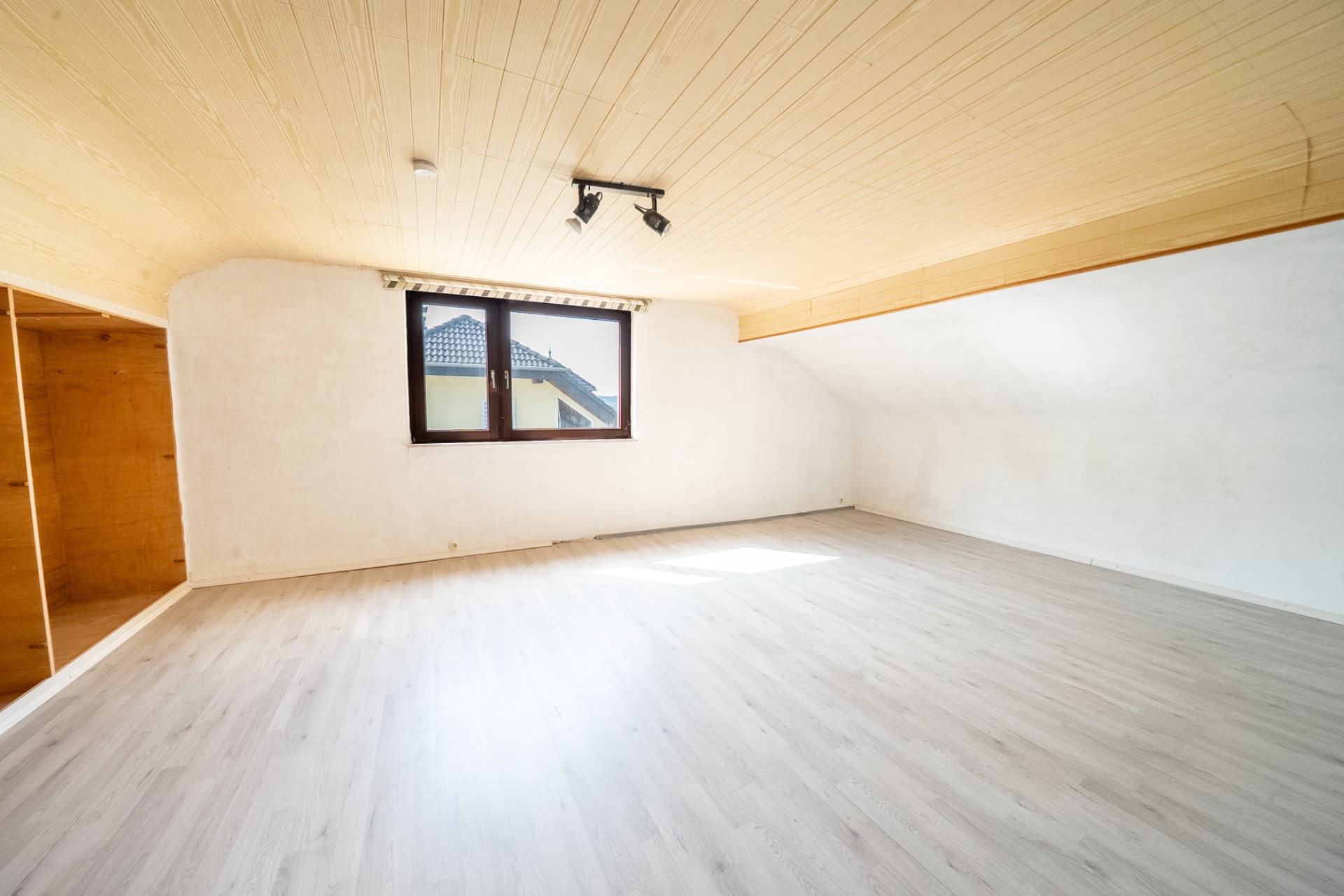 Heller leerer Dachbodenraum mit Holzdecke, Fenster und hellem Boden.