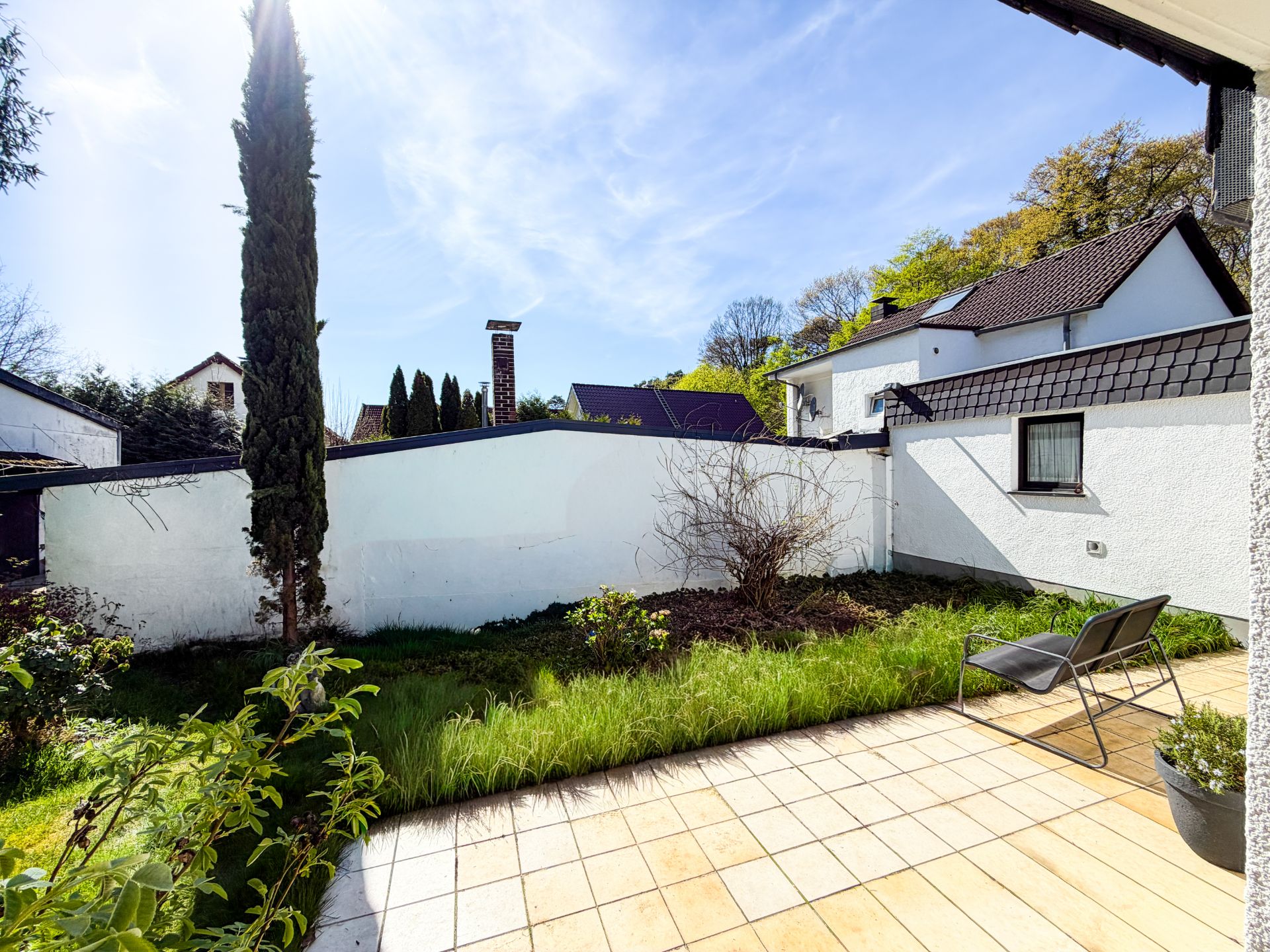 Geflieste Terrasse mit zwei Stühlen, angrenzender Rasen und Garten, umgeben von weißen Mauern.
