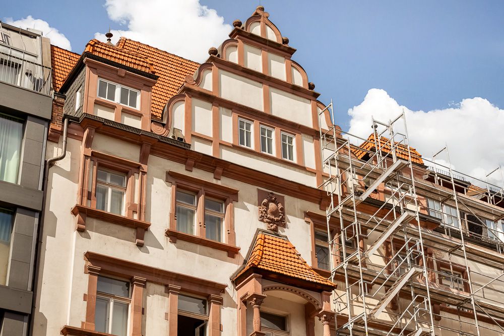 Fassade eines altmodischen Wohnhauses mit Gerüst an der Seite und roten Dachziegeln.