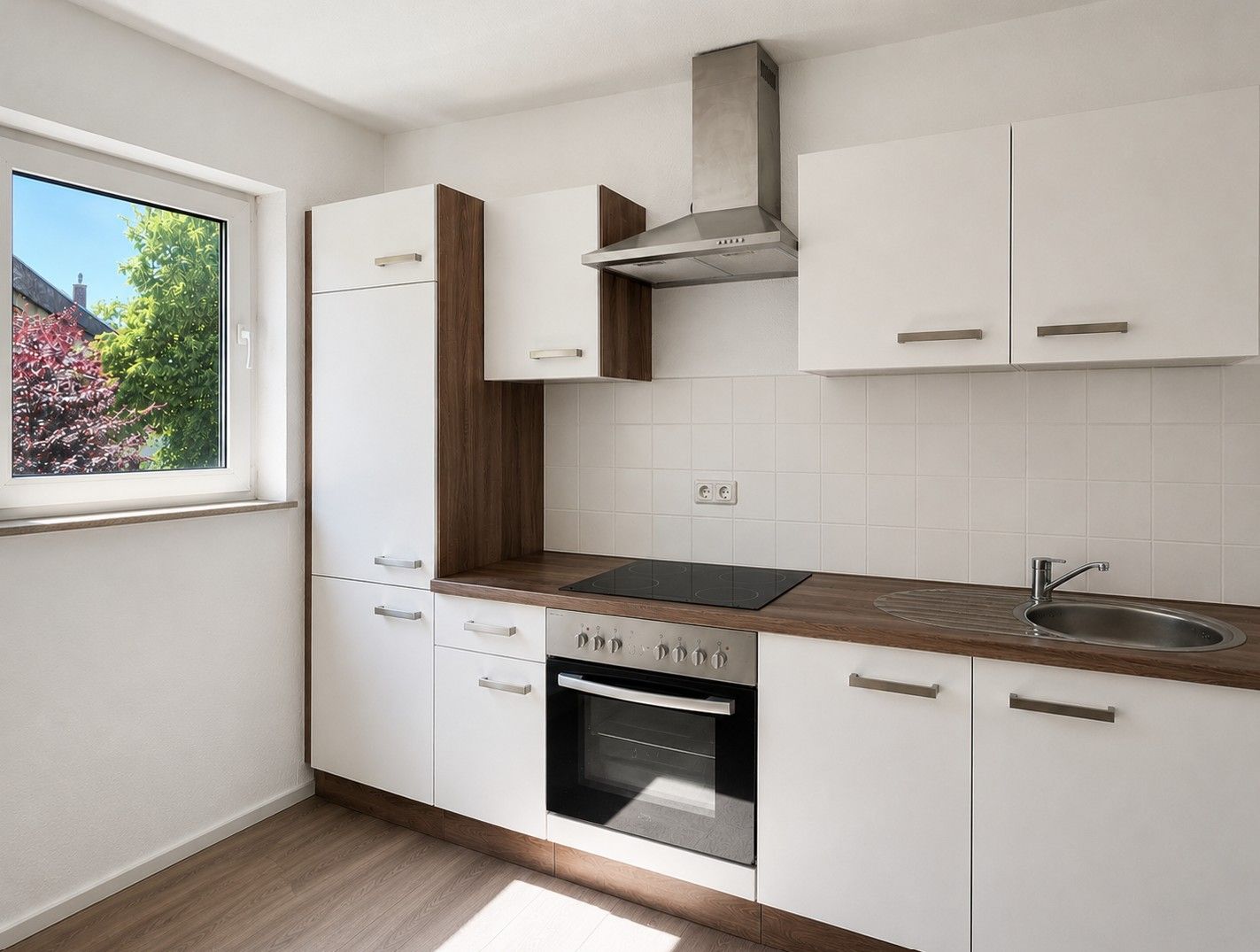 Moderne Einbauküche mit Herd, Spüle, weißen Schränken und Fenster.