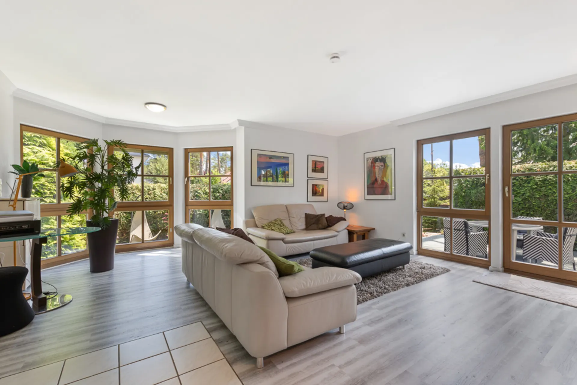 Helles Wohnzimmer mit großen Fenstern, Sofa, Pflanzen und Zugang zur Terrasse.
