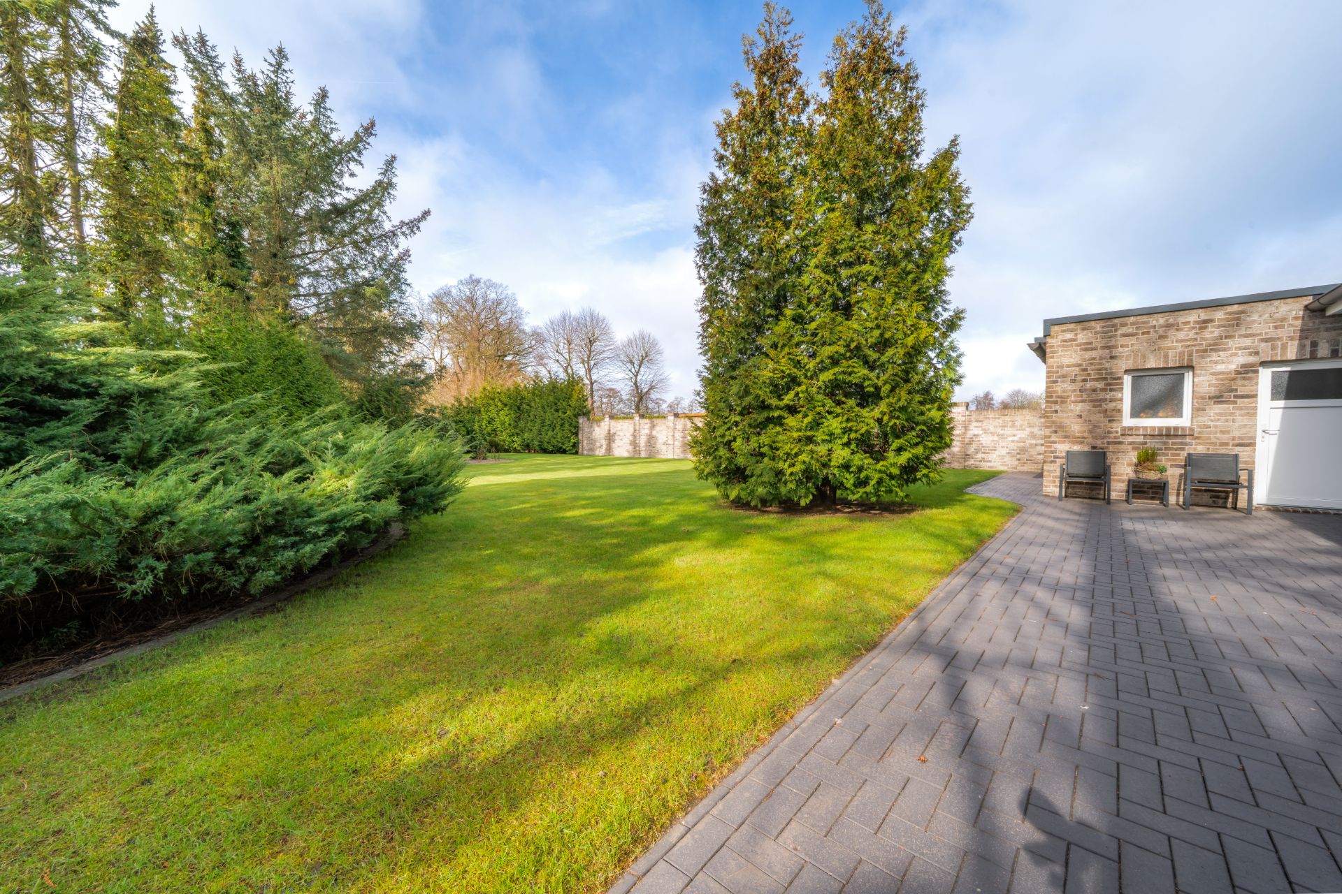 Garten mit Rasen, Bäumen und gepflastertem Weg neben einem Wohnhaus.