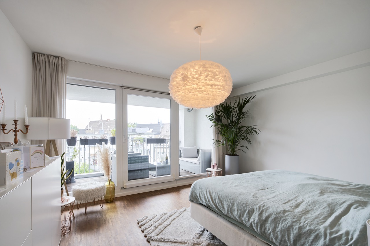 Helles Schlafzimmer mit großem Bett, runder Lampe, Balkon und viel Tageslicht.