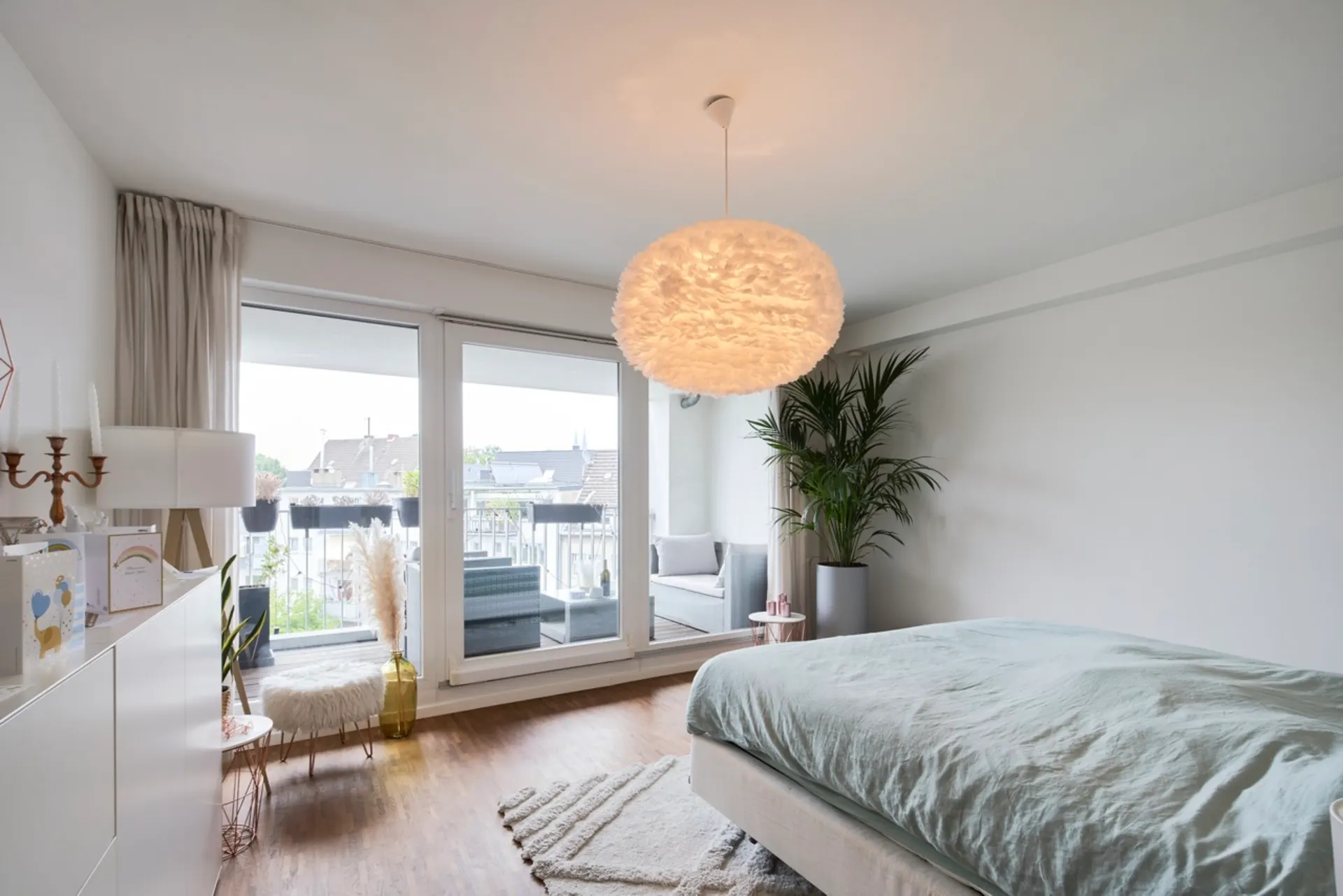 Helles Schlafzimmer mit großem Bett, runder Lampe, Balkon und viel Tageslicht.