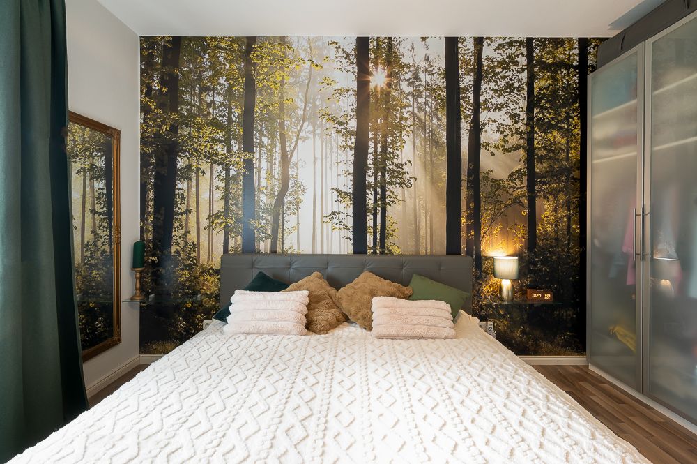 Schlafzimmer mit großem Bett und Wald-Fototapete an der Wand.