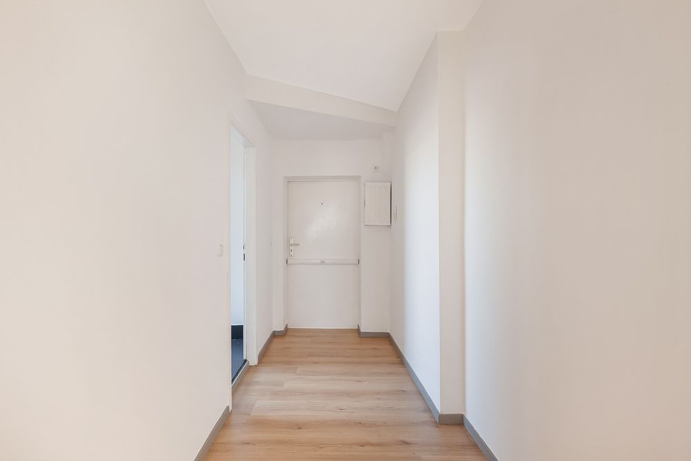 Heller Flur mit Holzboden, weißer Eingangstür und angrenzendem Raum.