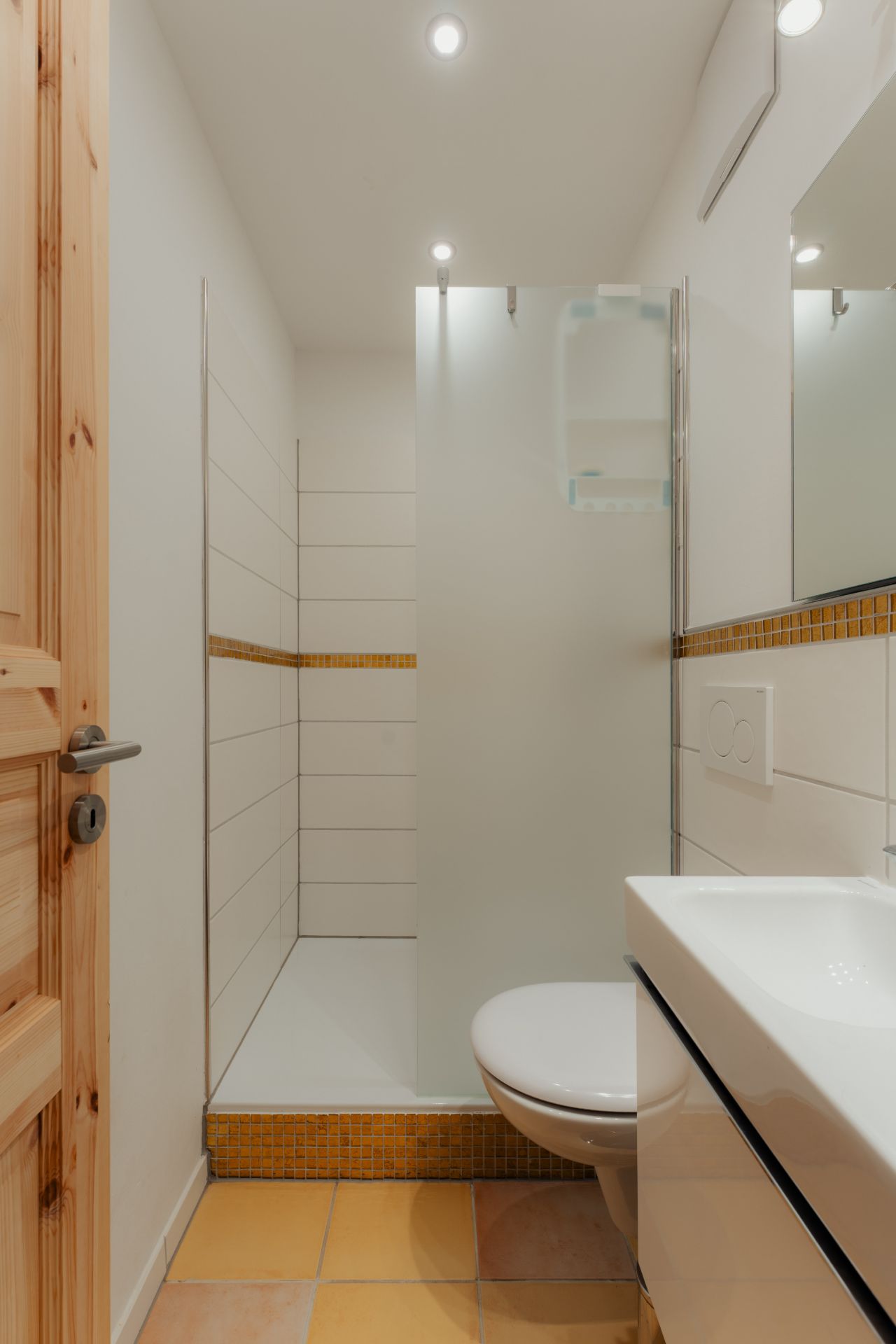 Modernes Bad mit Dusche, WC und Waschbecken, helle Fliesen und Holztür.