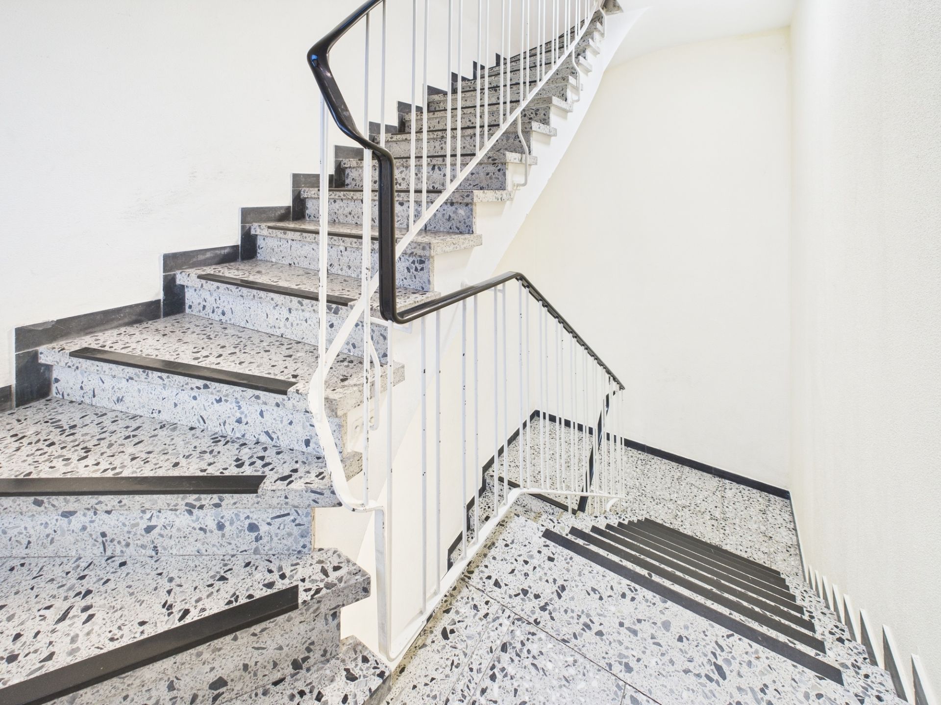 Treppenhaus mit grauen Steinstufen und weißem Geländer in einem Wohngebäude.