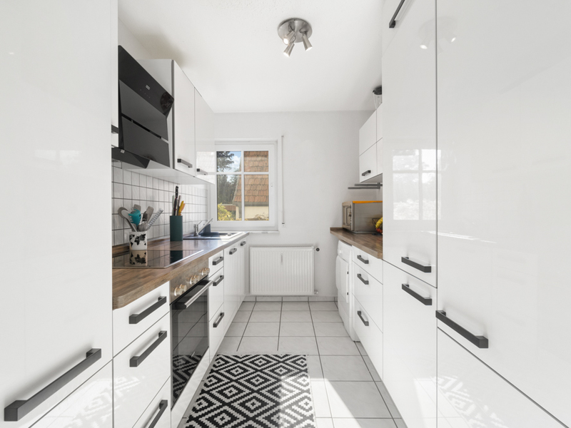 Moderne, weiße Einbauküche mit Holzarbeitsplatten und Fenster, Teppich auf Fliesenboden.