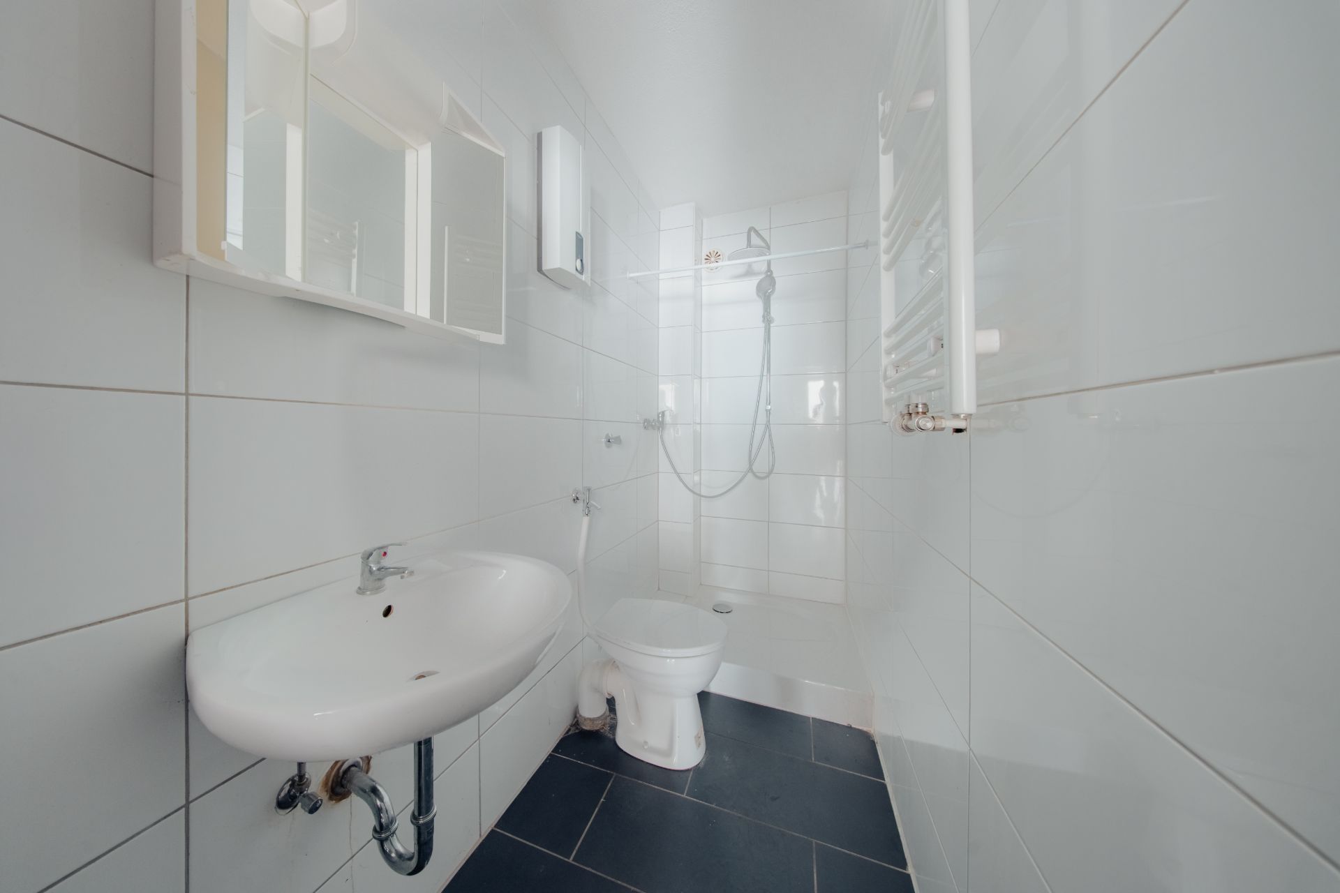 Modernes Badezimmer mit Waschbecken, Toilette und begehbarer Dusche, alles in weiß gefliest.