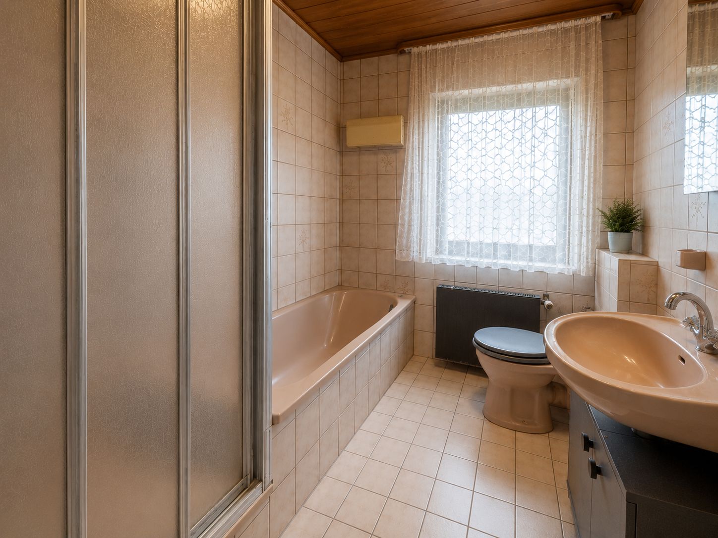Helles Badezimmer mit Badewanne, Dusche, Waschbecken und Toilette, Fenster mit Gardine.