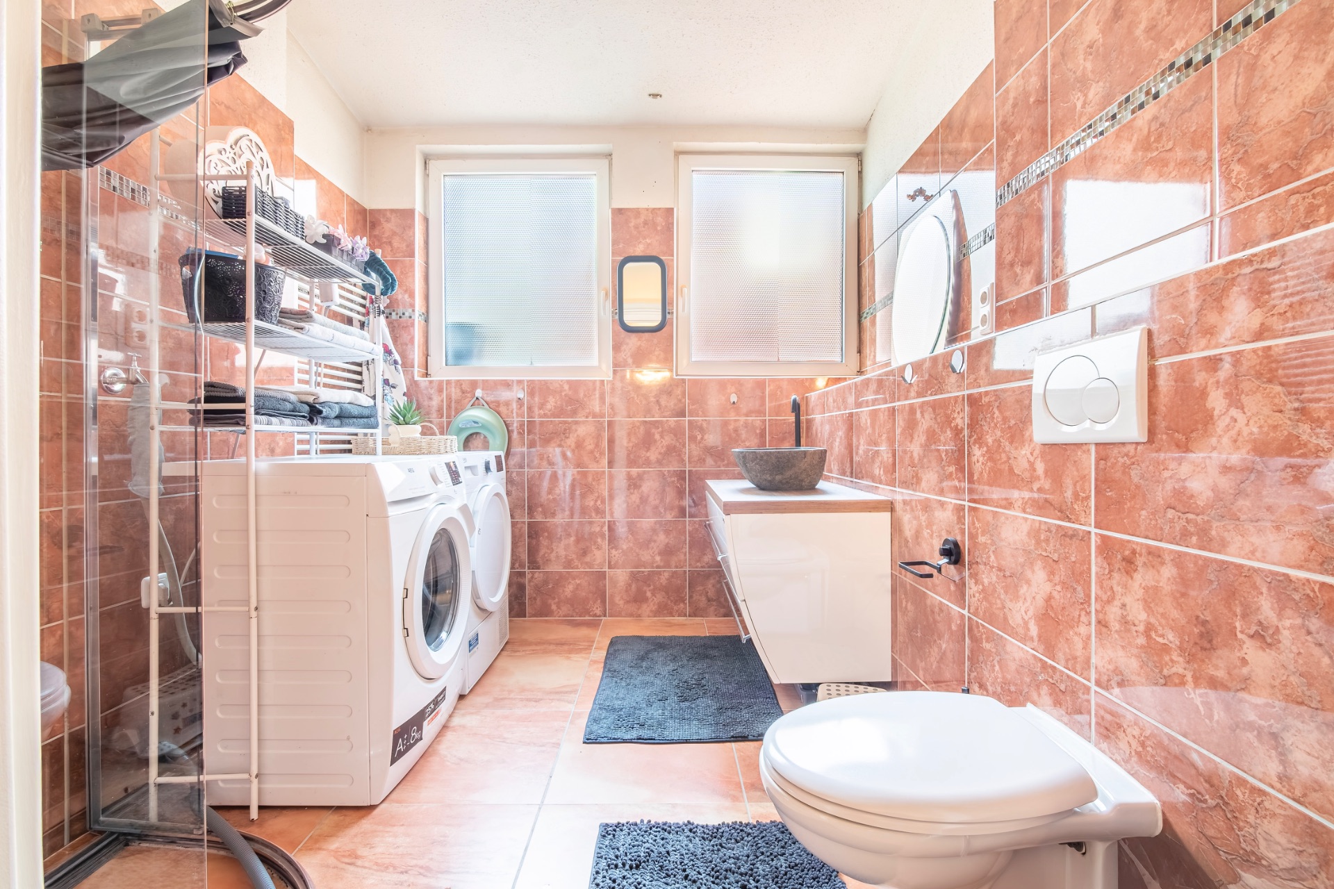 Modernes Bad mit Waschmaschine, Trockner, WC, Waschbecken und braunen Fliesen.