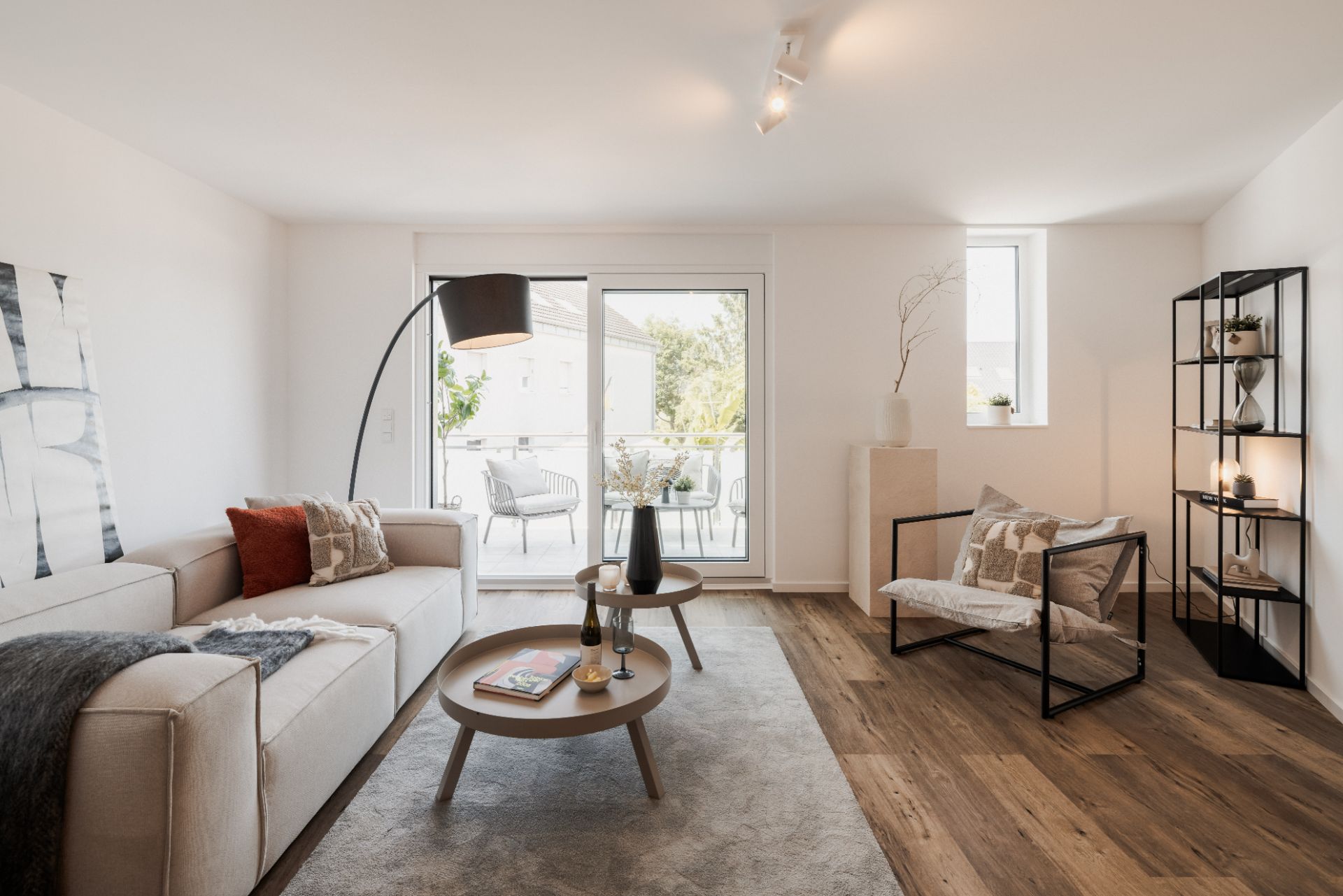Modernes Wohnzimmer mit Sofa, Sessel, Couchtischen und Zugang zum Balkon.