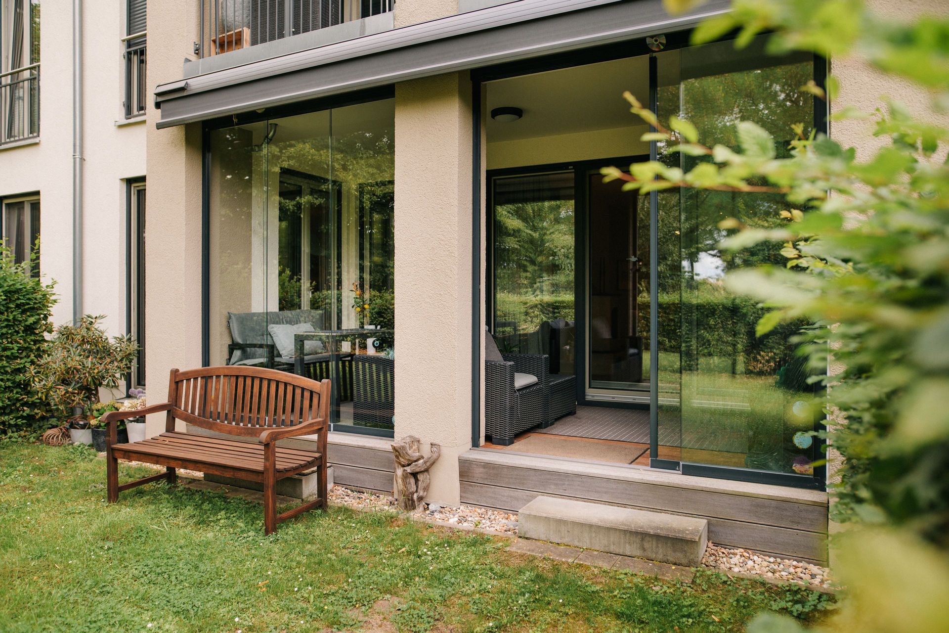 Terrasse mit Glastüren, Holzbänkchen und Garten im Vordergrund.