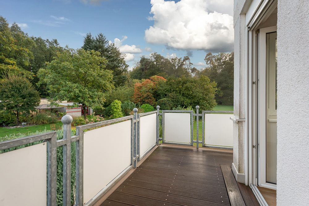 Balkon mit Holzboden und Metallgeländer, Blick auf grünen Garten und Bäume.