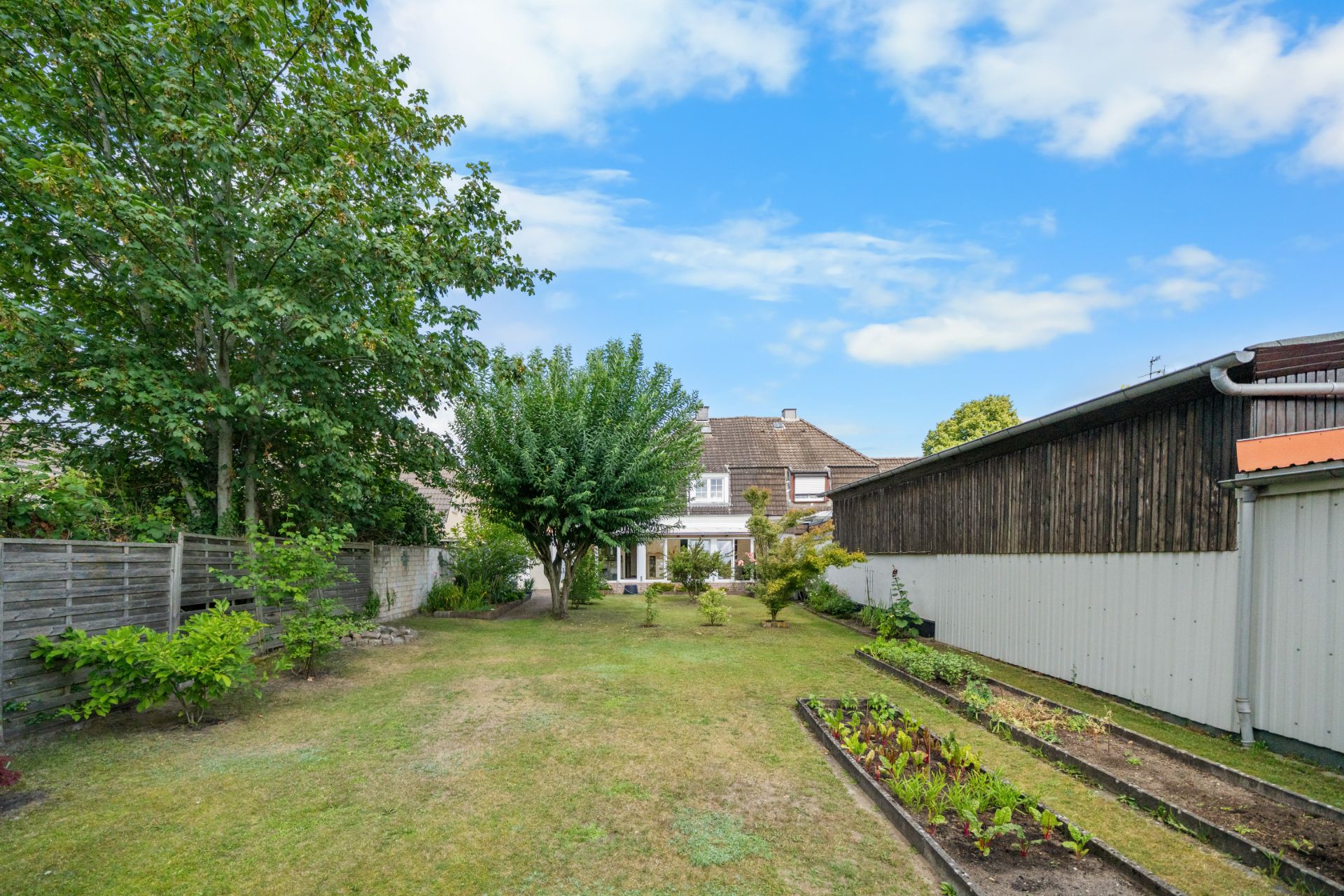 Garten mit Rasen, Bäumen, Beeten und Haus im Hintergrund.