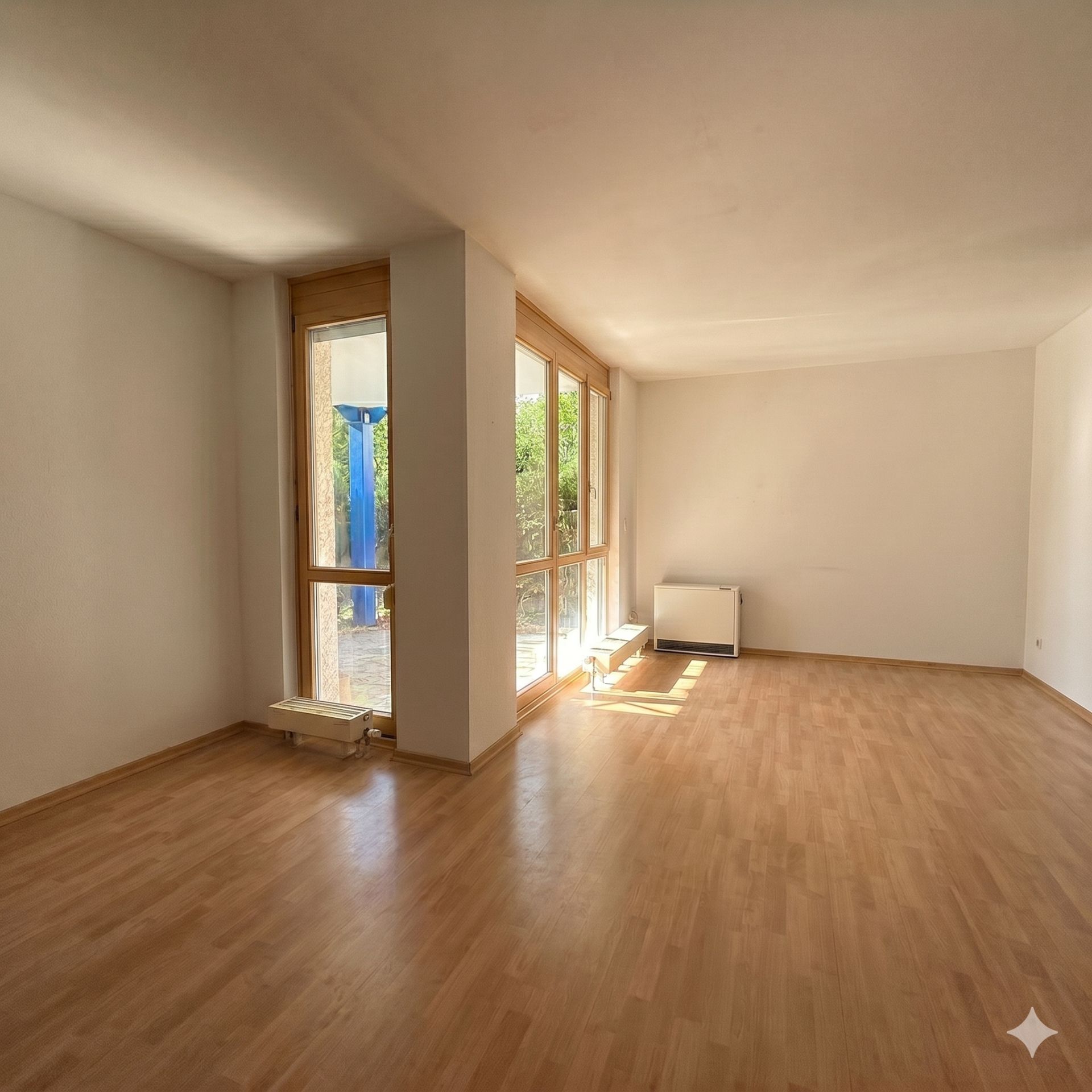 Helles leeres Wohnzimmer mit großen Fenstern und Parkettboden.