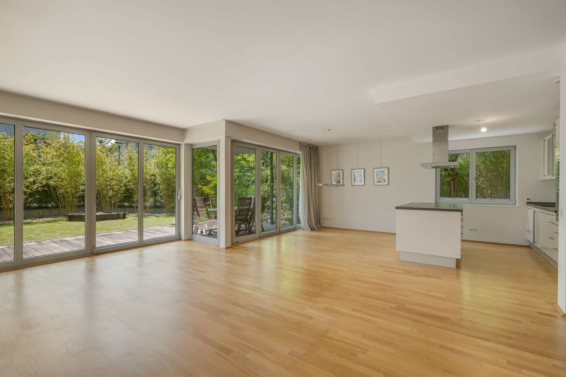 Heller Wohnraum mit Parkettboden, großer Fensterfront und offener Küche, Blick auf Terrasse und Garten.