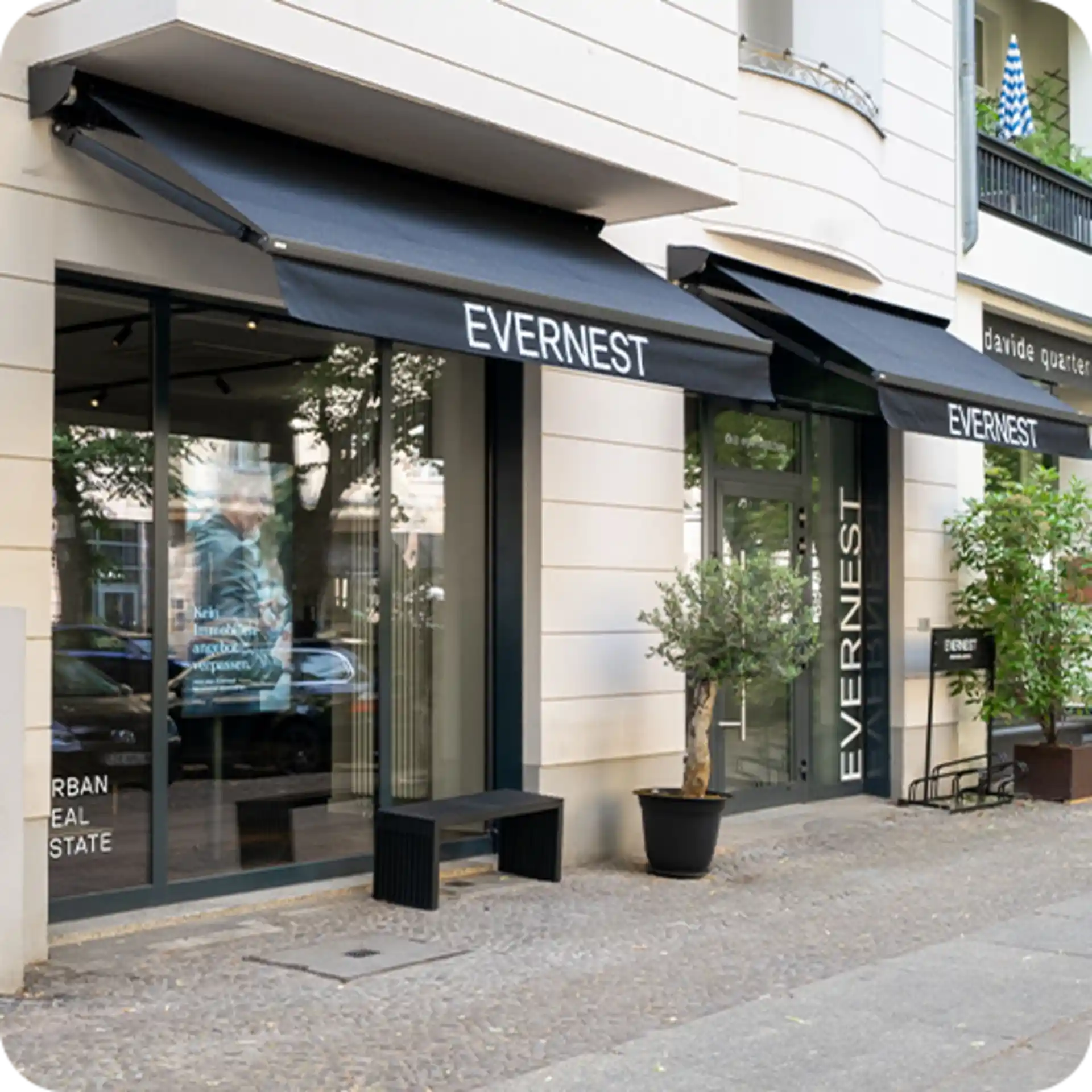 Moderne Hausfassade mit zwei Glas-Eingangstüren, schwarzen Markisen und einem kleinen Baum im Topf.