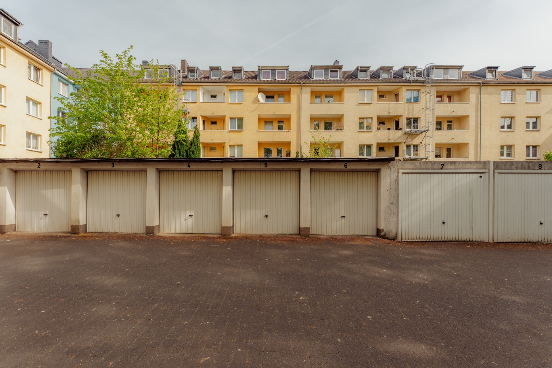 Mehrere Garagentore vor einem gelben Mehrfamilienhaus mit Balkonen und Fenstern.