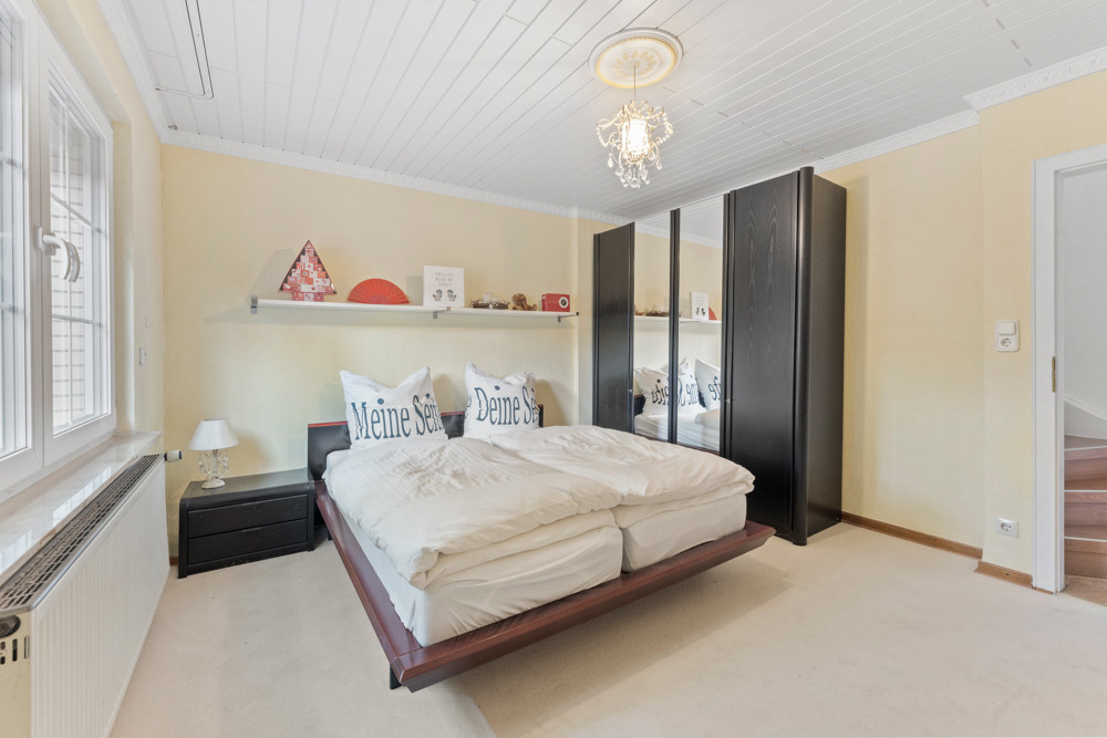 Helles Schlafzimmer mit Doppelbett, schwarzem Kleiderschrank und Regal mit Dekorationen an der Wand.