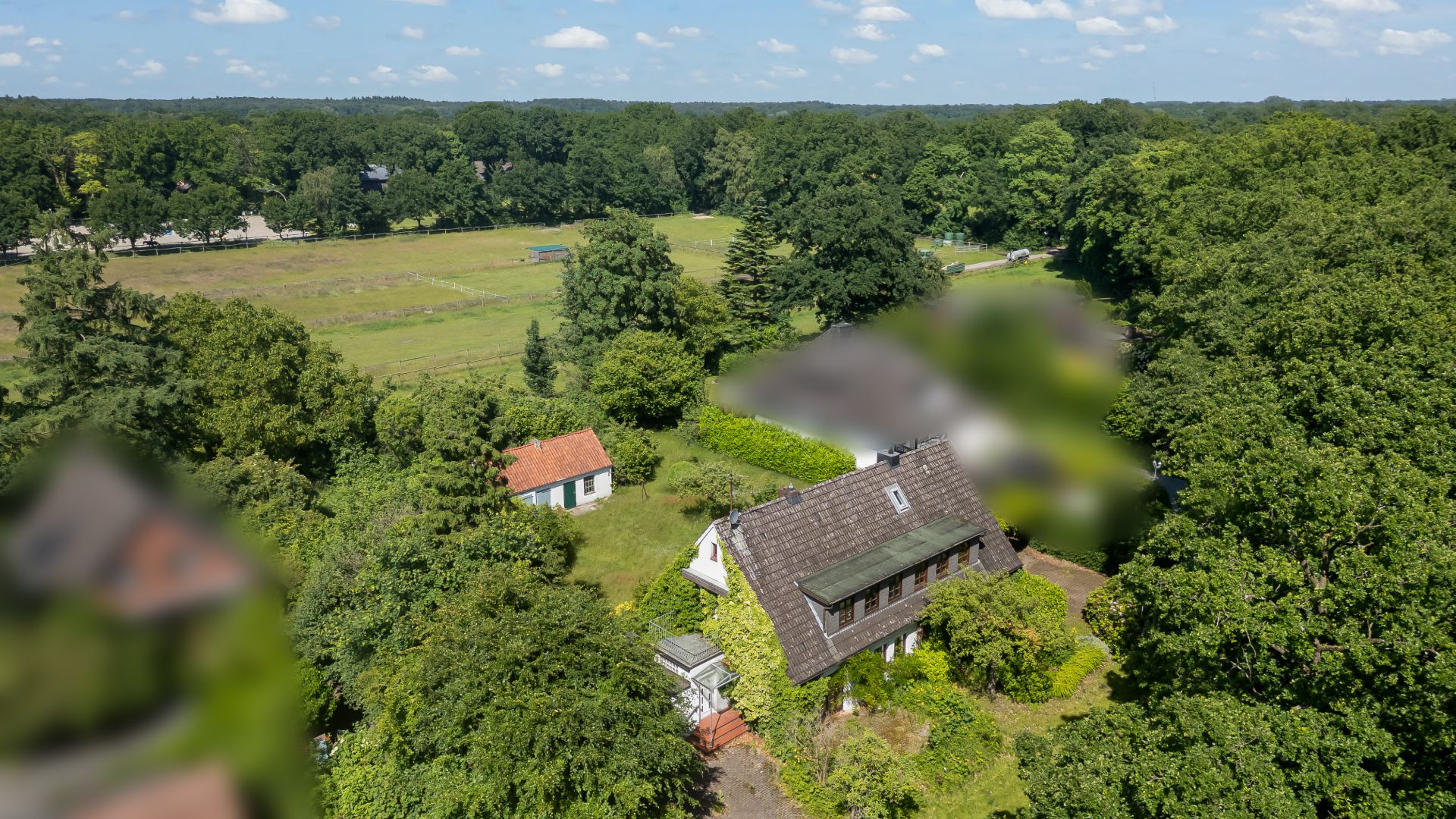Luftaufnahme eines Hauses mit Garten, umgeben von Bäumen und einer Wiese.