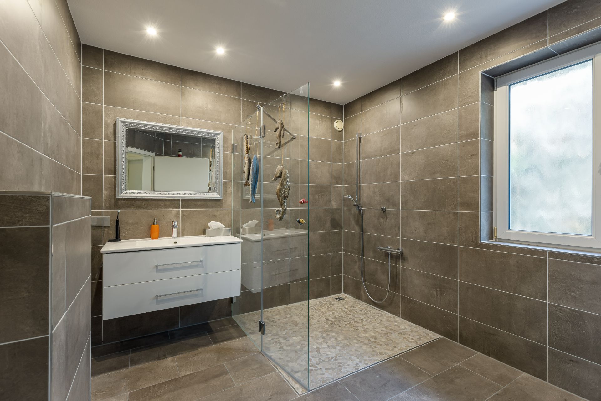 Modernes Badezimmer mit bodengleicher Dusche, Waschbecken und großem Fenster.