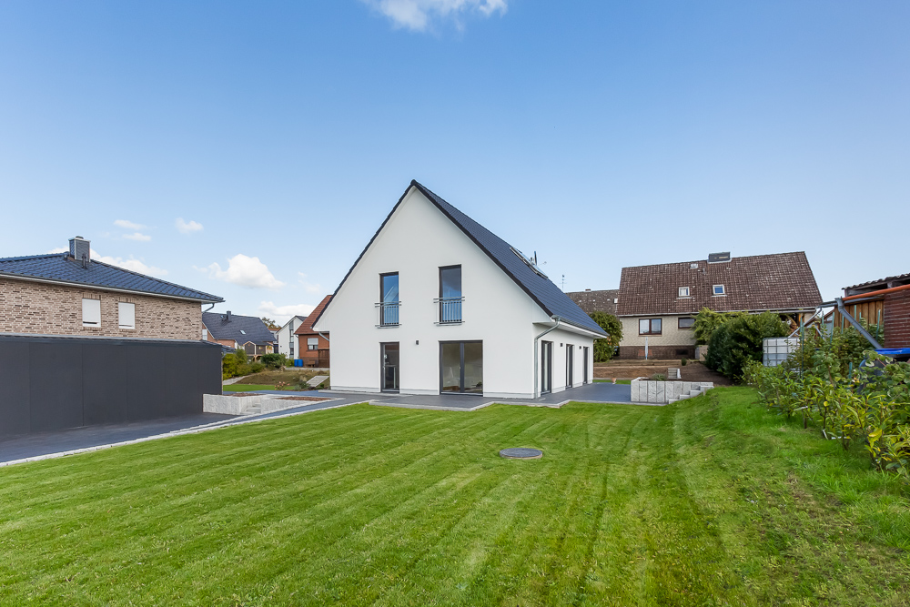 Modernes weißes Einfamilienhaus mit spitzem Dach und großem Rasen im Vordergrund.