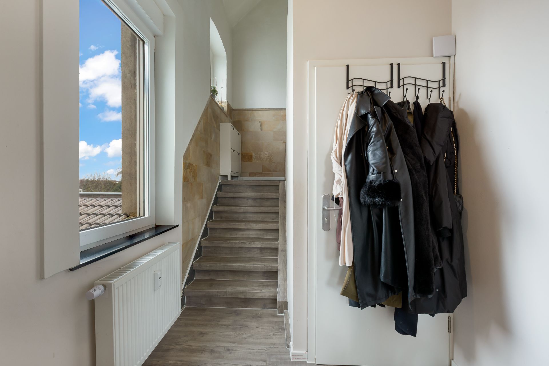 Flur mit Fenster, Heizung, Treppe und mehreren Jacken an der Tür.