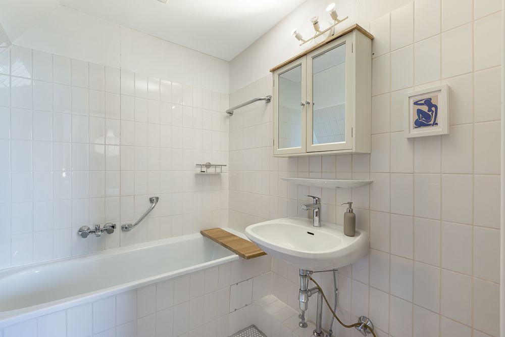 Helles Badezimmer mit Badewanne, Waschbecken und Spiegelschrank an weiß gefliester Wand.