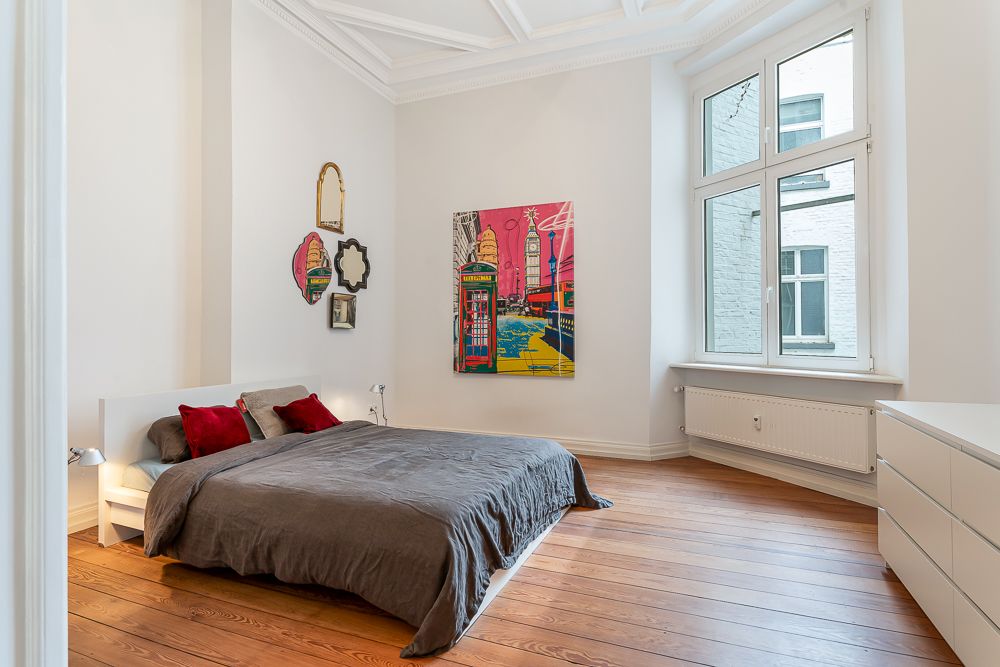 Helles Schlafzimmer mit Doppelbett, Holzfußboden, großem Fenster und bunter Wandkunst.