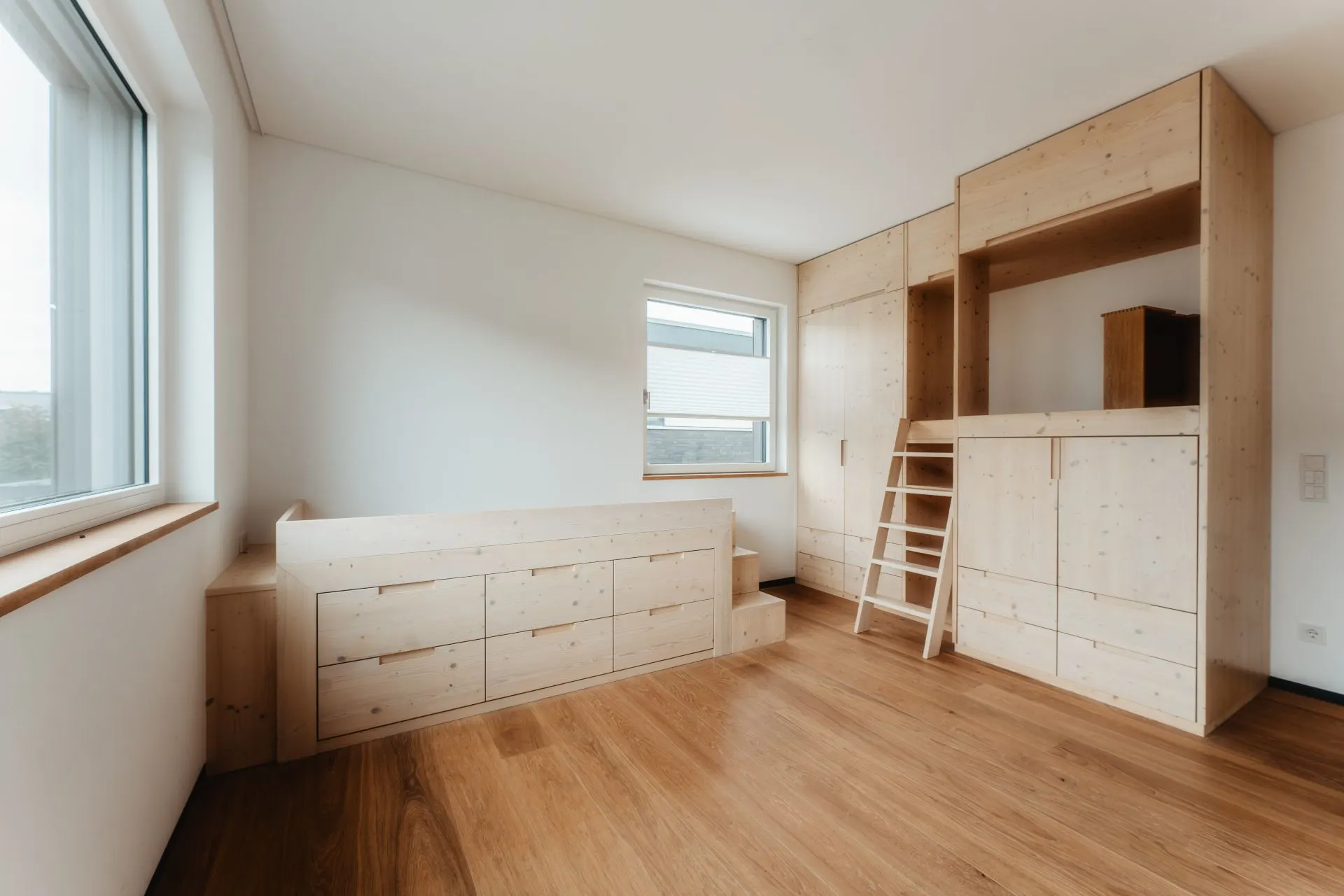 Helles Zimmer mit Holzboden, Einbaumöbeln, Bett mit Schubladen und Hochbett mit Leiter.