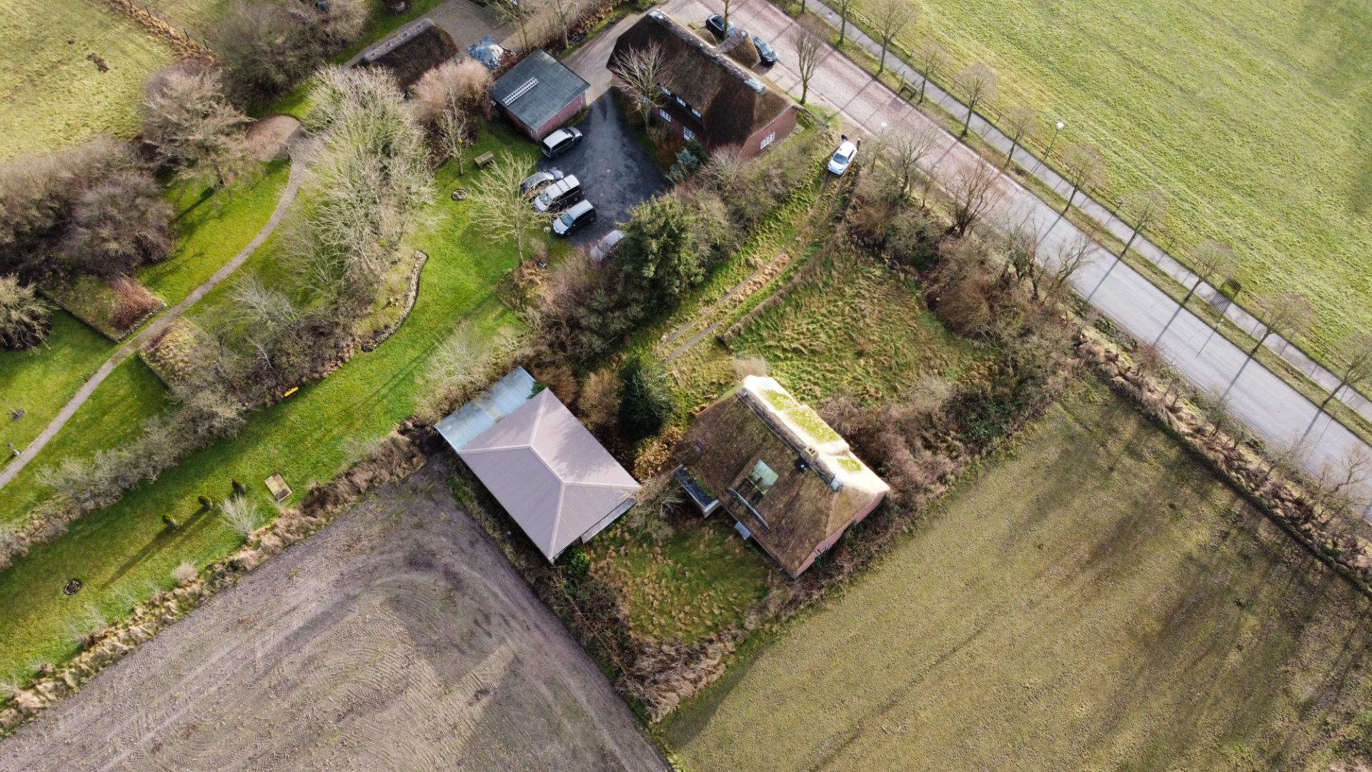 Luftaufnahme eines Hauses mit Nebengebäude, umgeben von Feldern und einer Straße.